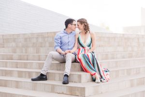 Couple sitting together on concrete steps with downtown buildings in background.