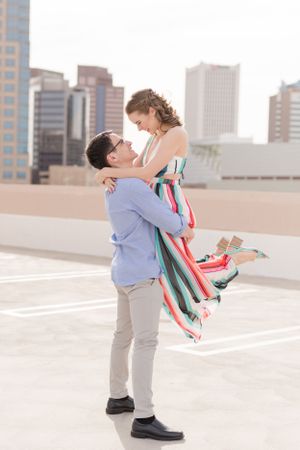 Romantic lift pose on urban rooftop with colorful striped dress flowing in the breeze.