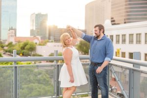 Couple sharing a playful moment on rooftop deck with urban skyline backdrop at sunset.