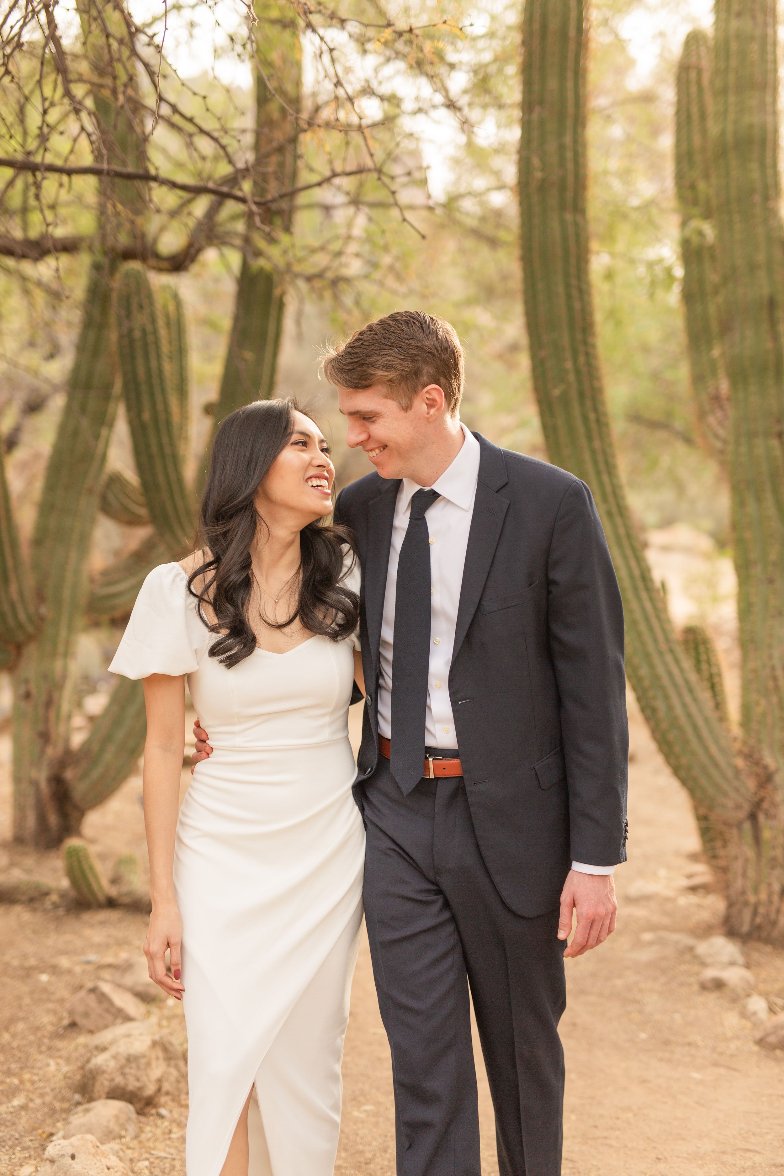 A couple shares a romantic moment on a desert trail surrounded by towering saguaro cacti.
