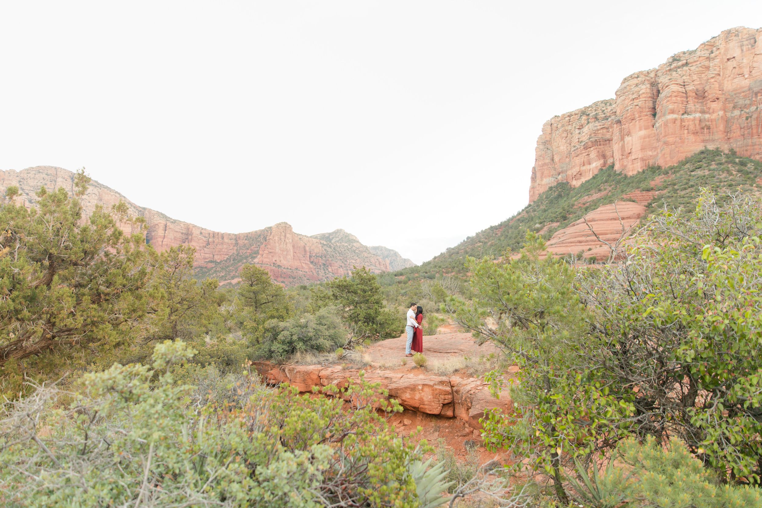 Couple standing together on red rocks with majestic Sedona mountains in background.