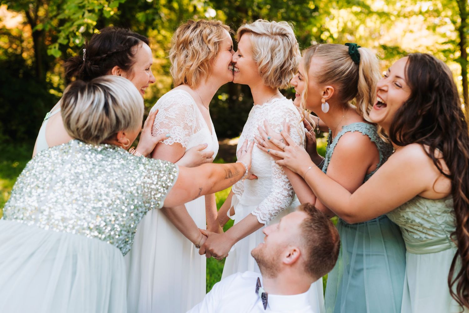 Wedding party in pastel dresses shares joyful moment outdoors in golden sunlight.