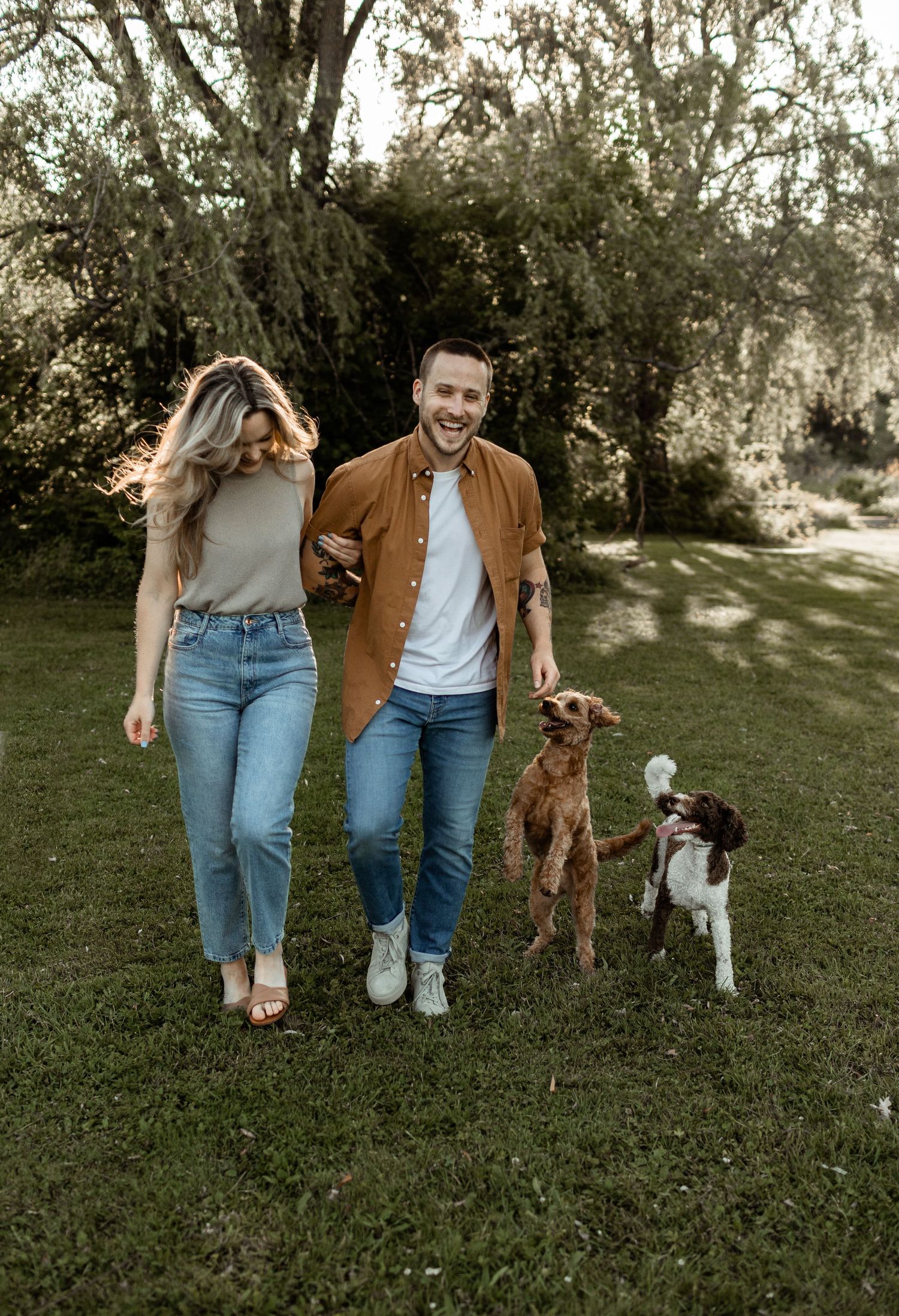 A carefree couple walking with their two dogs on a grassy lawn on a sunny day.