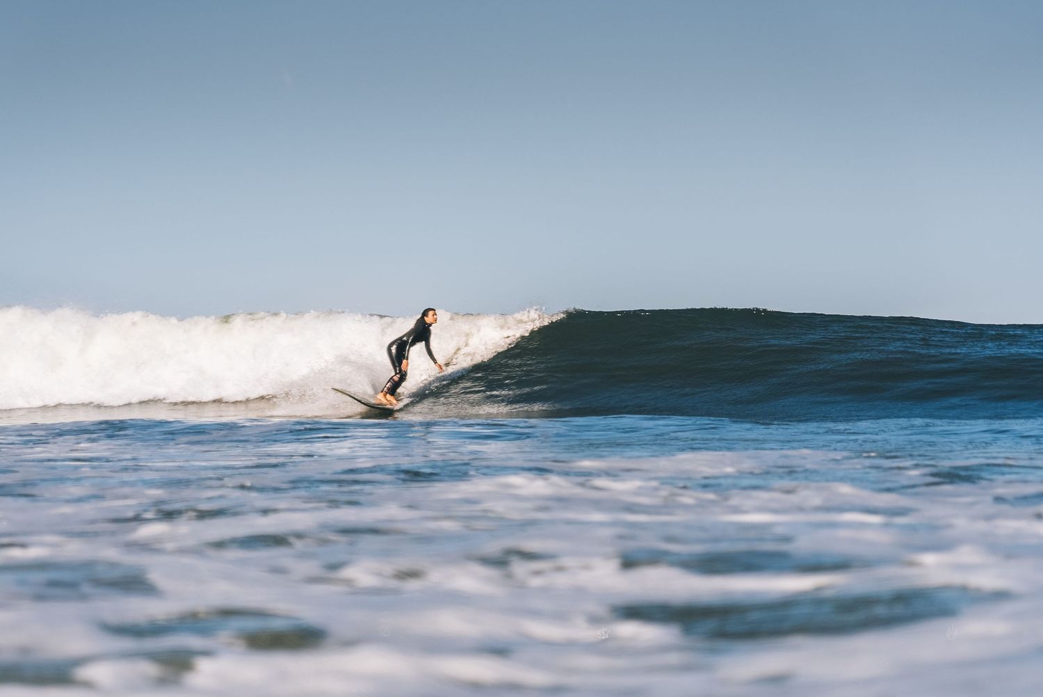 Silhouette of a surfer riding a breaking ocean wave during daytime.