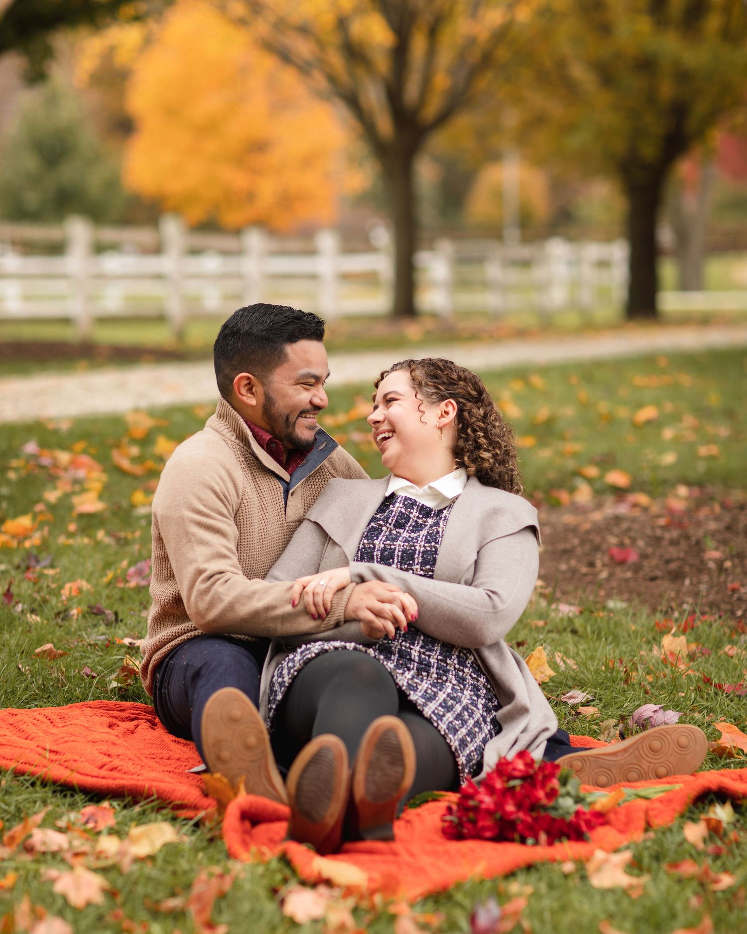 A romantic autumn picnic scene with a couple laughing together on an orange blanket surrounded by fall foliage.