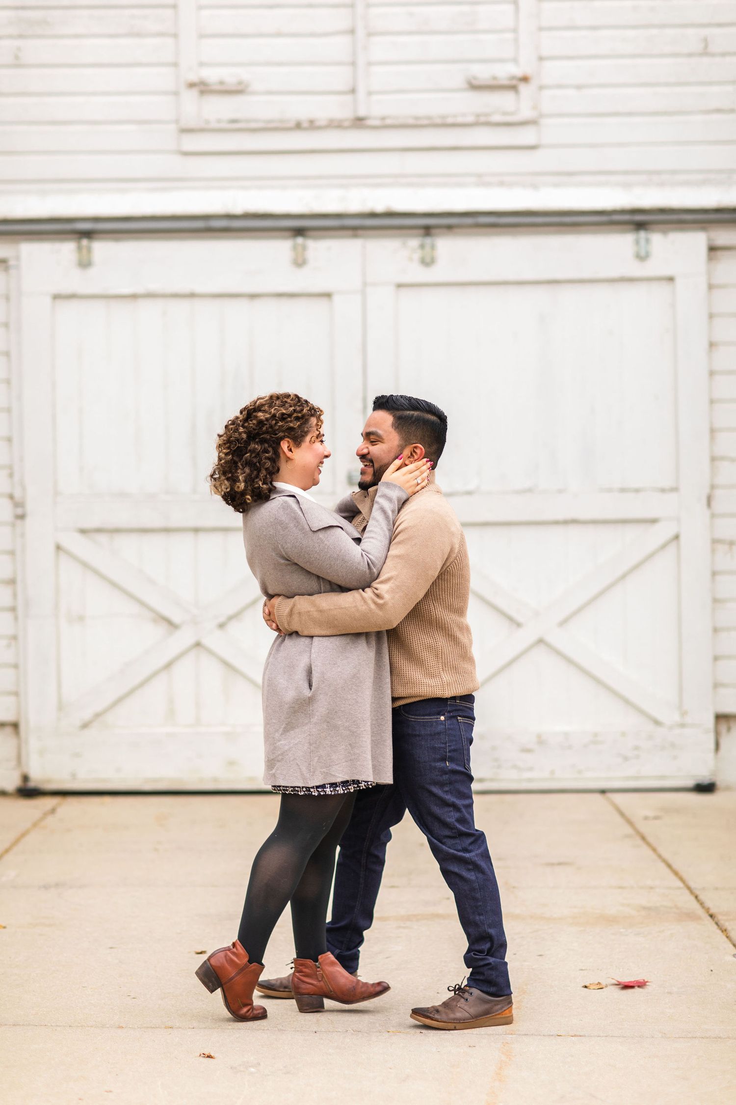 A tender moment between a couple embracing in front of a white barn door.