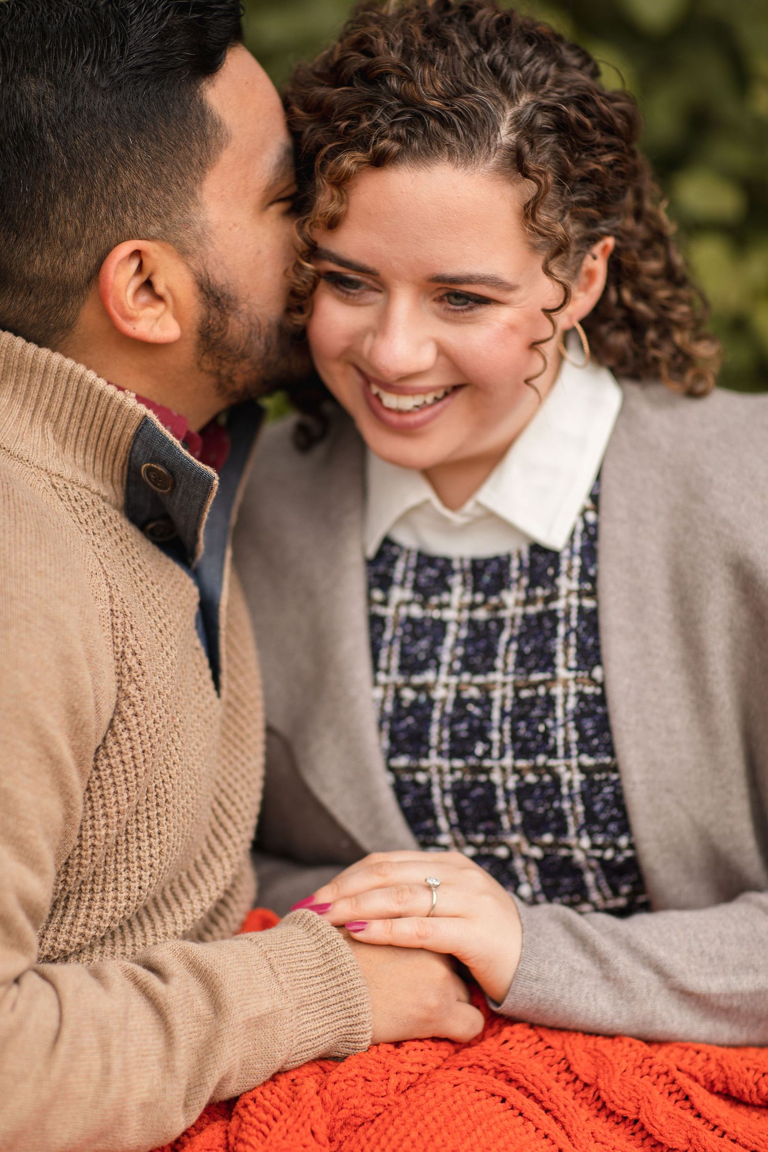 An intimate moment captured between a couple sharing laughter on an orange blanket outdoors.