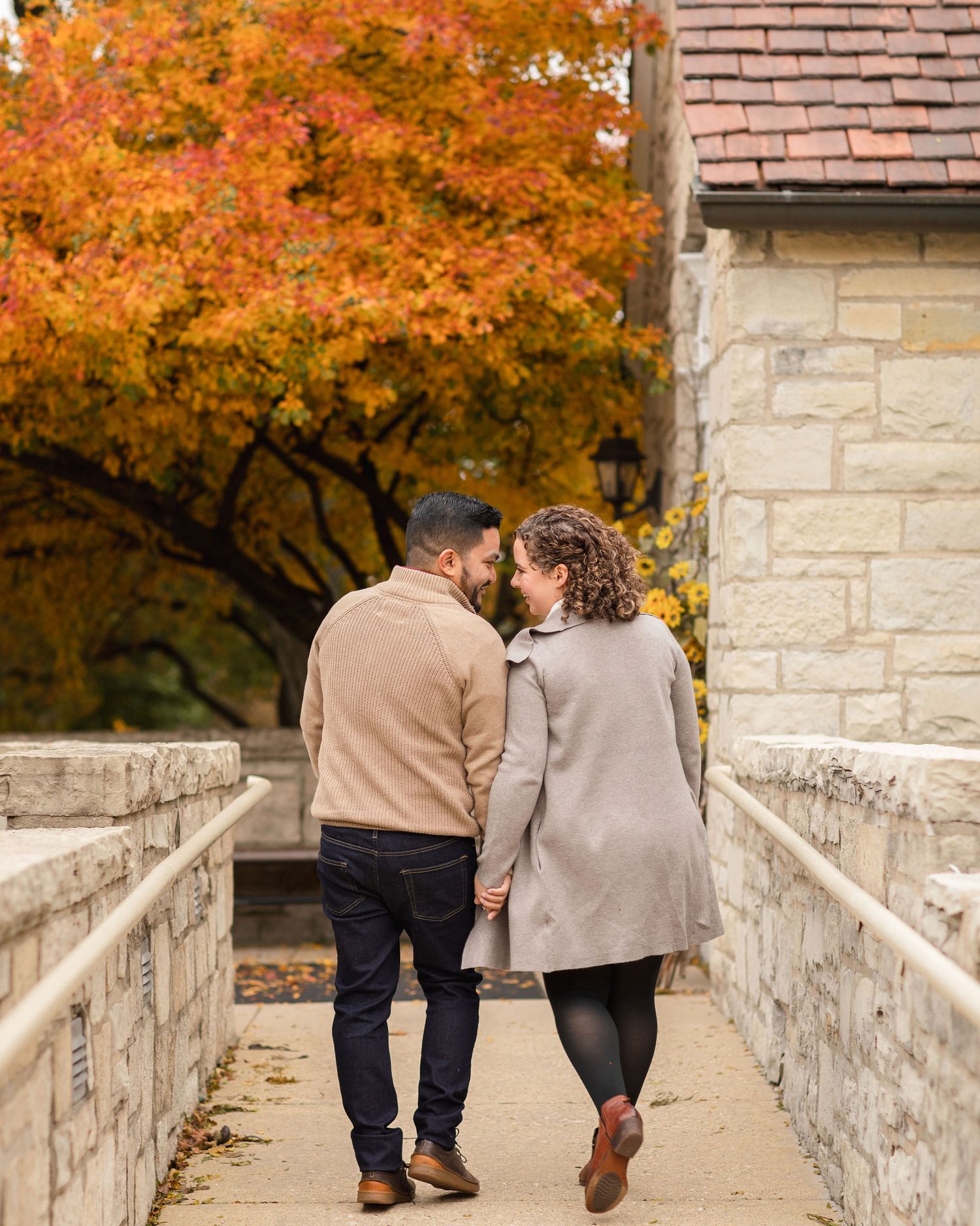 A couple walking together on a stone bridge with beautiful fall foliage in the background.