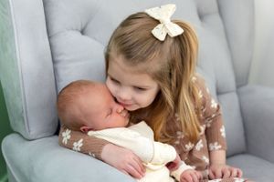 Newborn Photoshoot in Columbus featuring sister and baby brother cuddling on chair