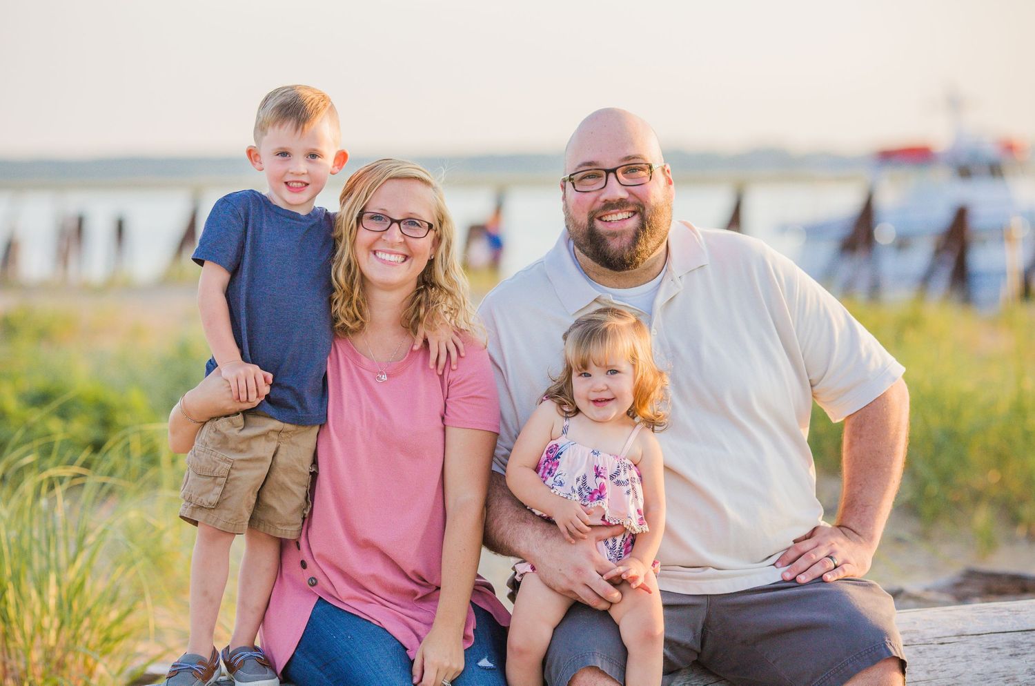 Happy family of four posing together at sunset near a beach boardwalk.