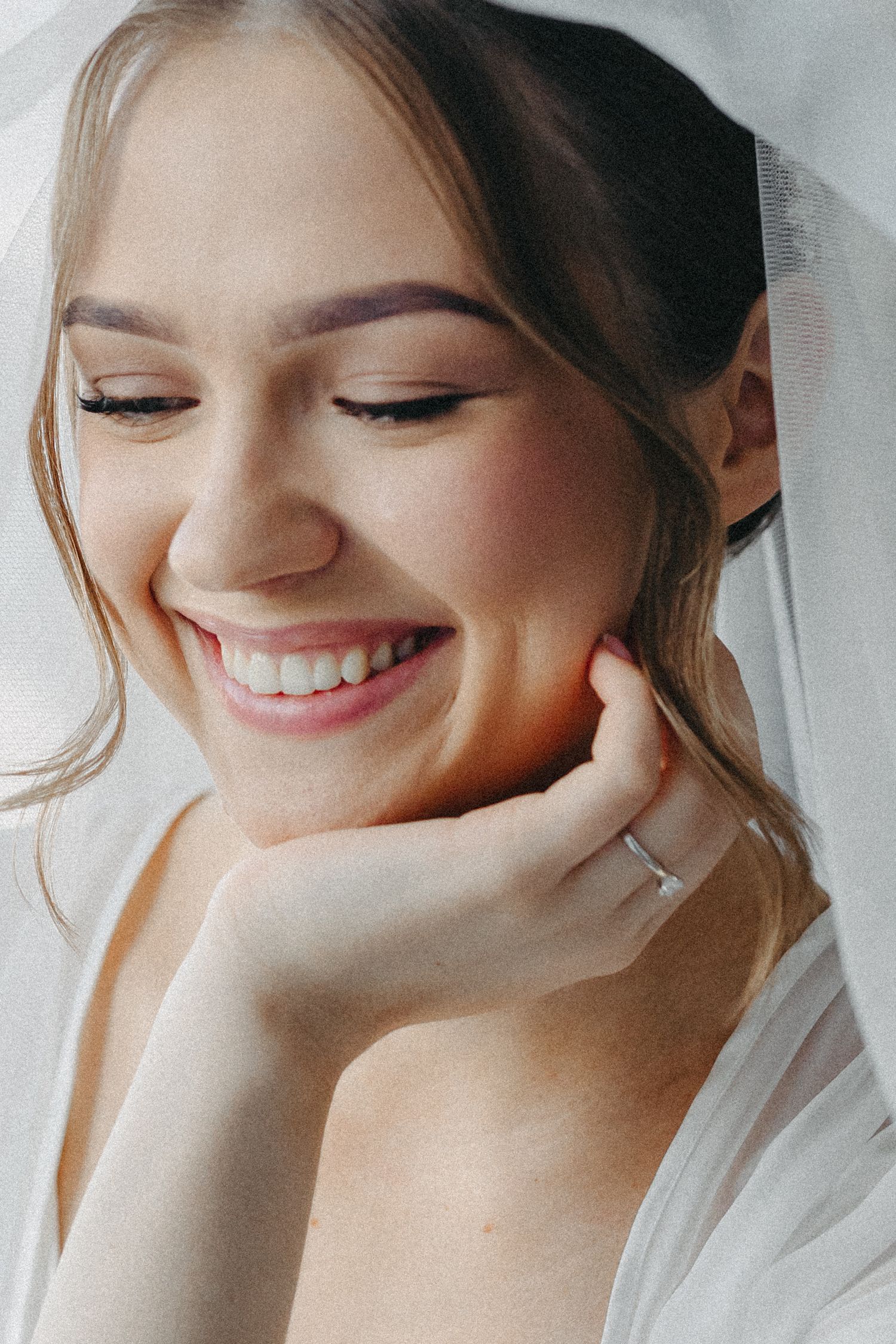 Close up portrait showing a joyful smile and natural bridal makeup with soft lighting and white veil.