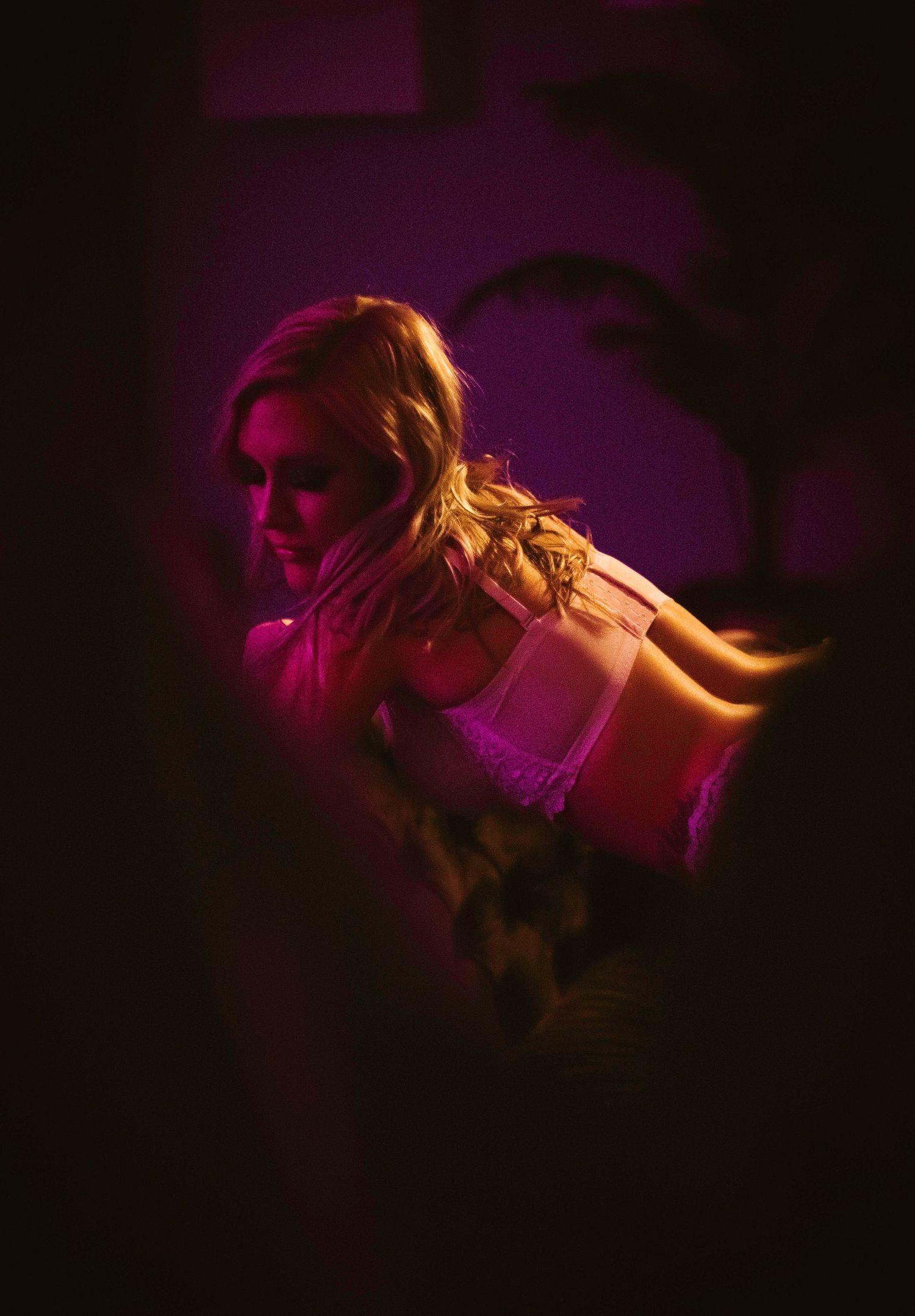 Moody boudoir portrait with pink lighting and dramatic shadows.
