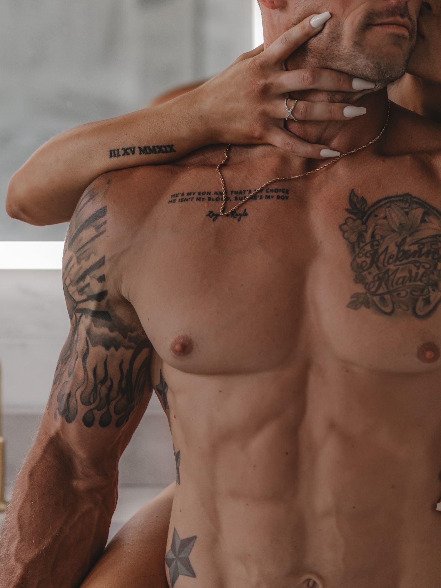 Close-up of tattooed torso with hand placement showing script tattoos and detailed artwork.