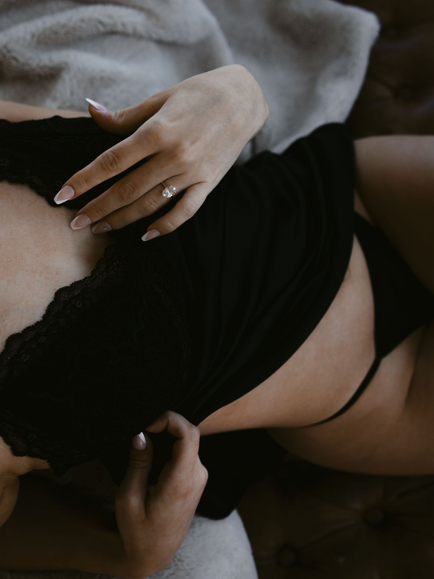 Artistic boudoir photo showing hand with engagement ring on black lace garment.