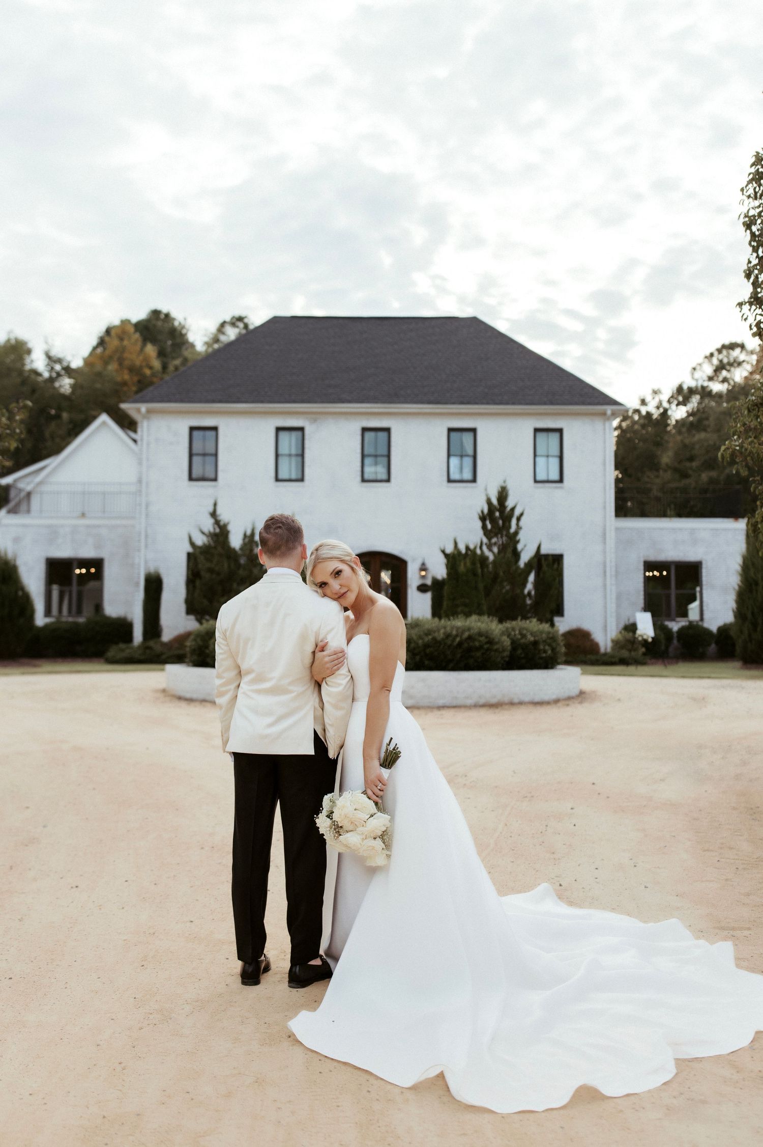 Bride and groom pose in front of a elegant white mansion with trailing wedding dress.