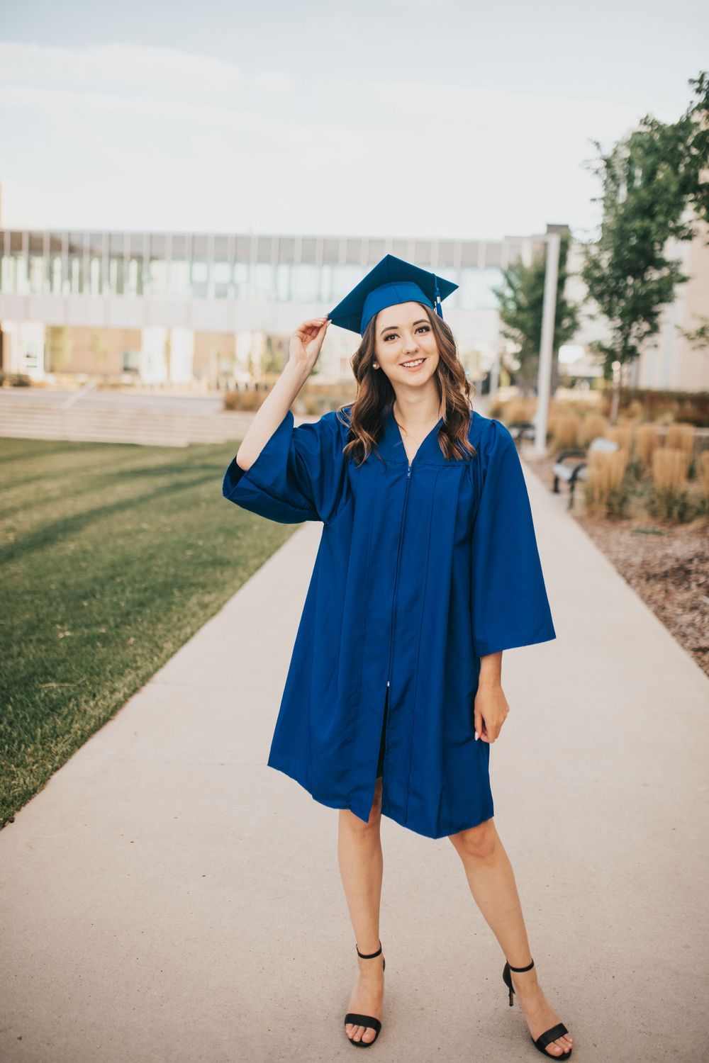 Girl wearing blue cap and gown standing on a pathway holding her graduation cap
