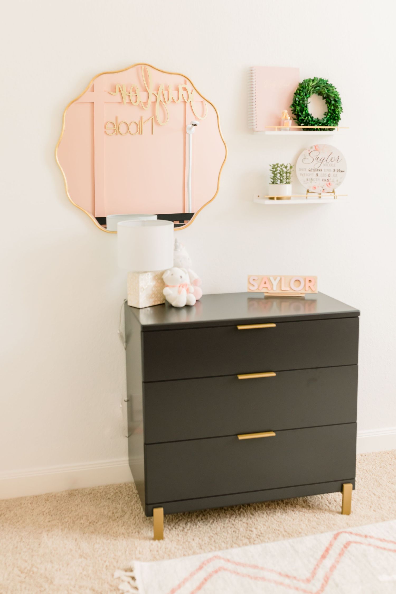 Black dresser with gold handles and pink wall decor in stylish nursery setting.