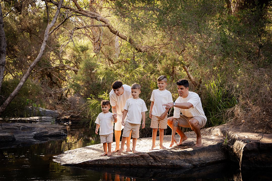 Family group gathered on rocky outcrop by peaceful water's edge in natural setting.