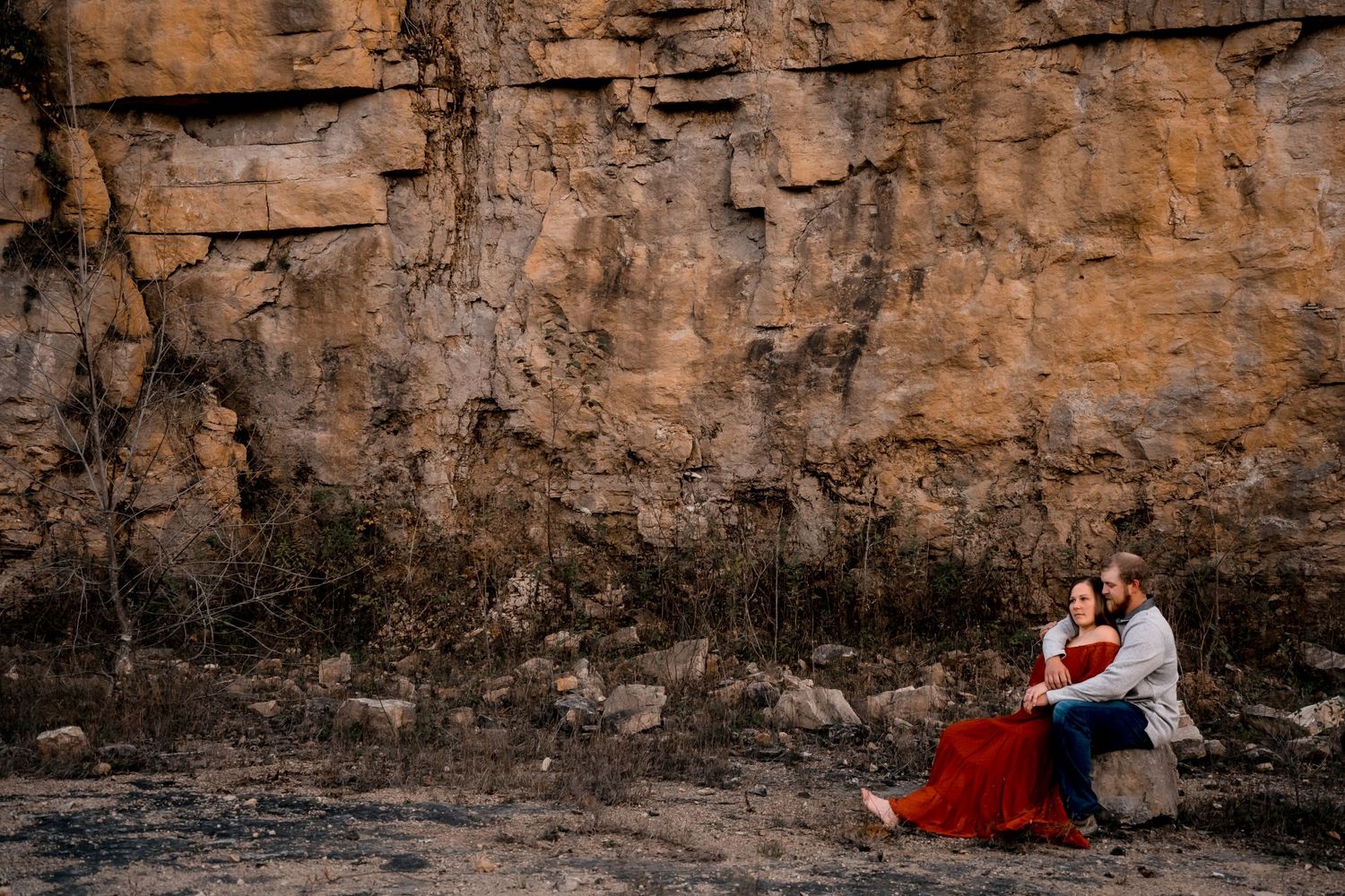 Couple in formal attire embracing against dramatic rocky cliff wall.