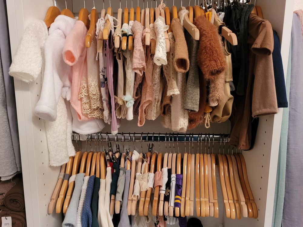 Closet rack displaying soft pastel and neutral colored clothing on wooden hangers.