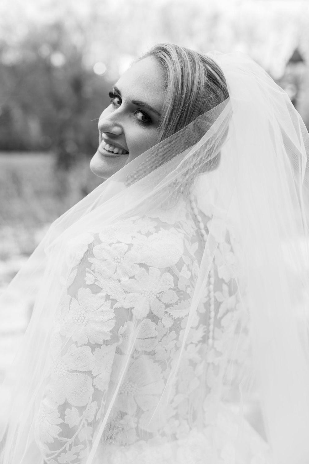 Black and white portrait of bride wearing veil and lace dress with joyful expression.