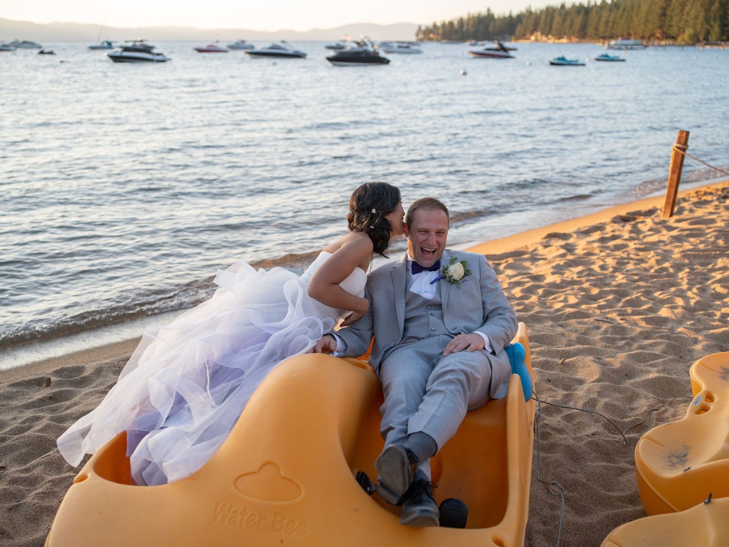 A couple shares a romantic moment on a yellow kayak at a beach during golden hour, with boats in the background.
