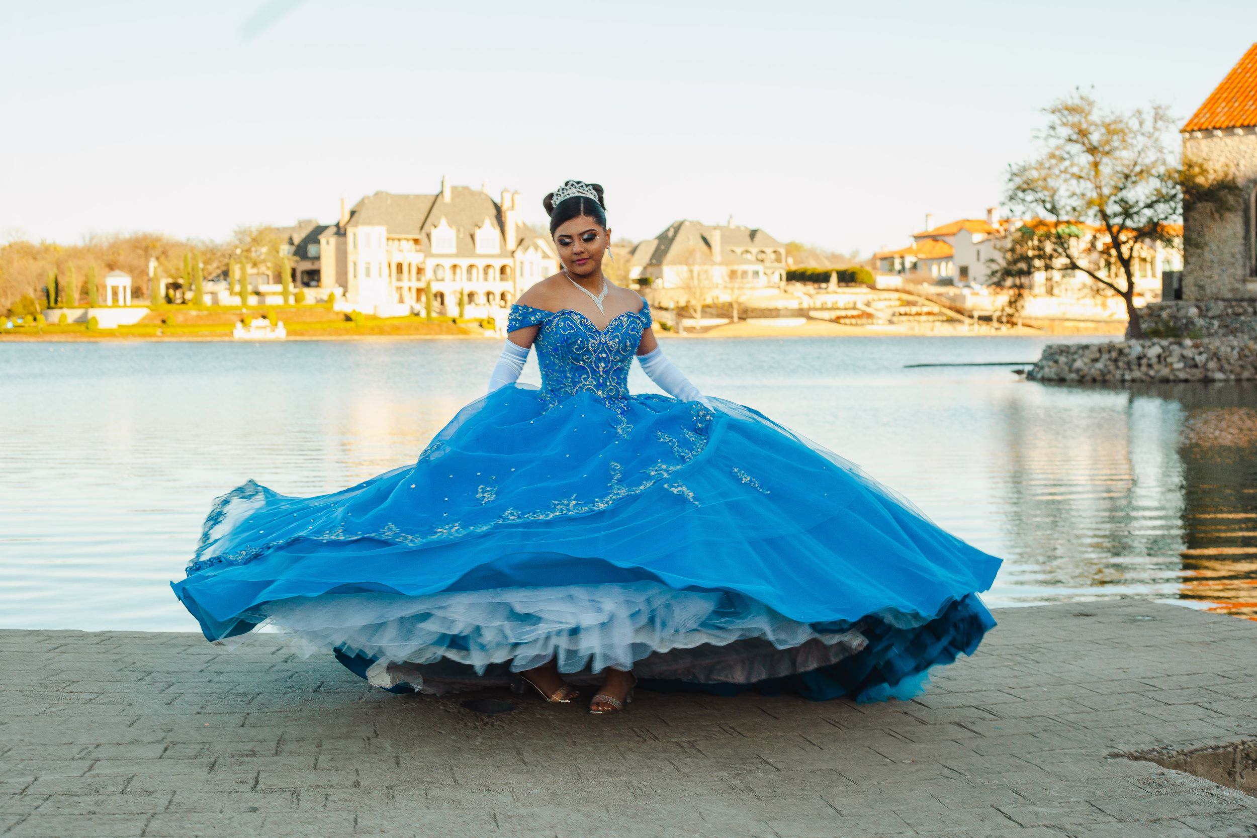 A flowing blue ballgown silhouetted against a waterfront landscape.
