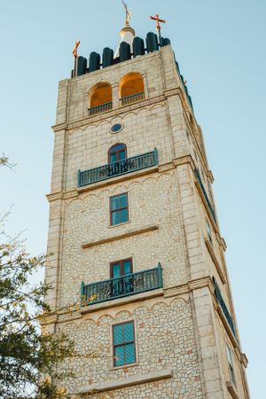 Stone church tower with arched windows and green shutters against blue sky.