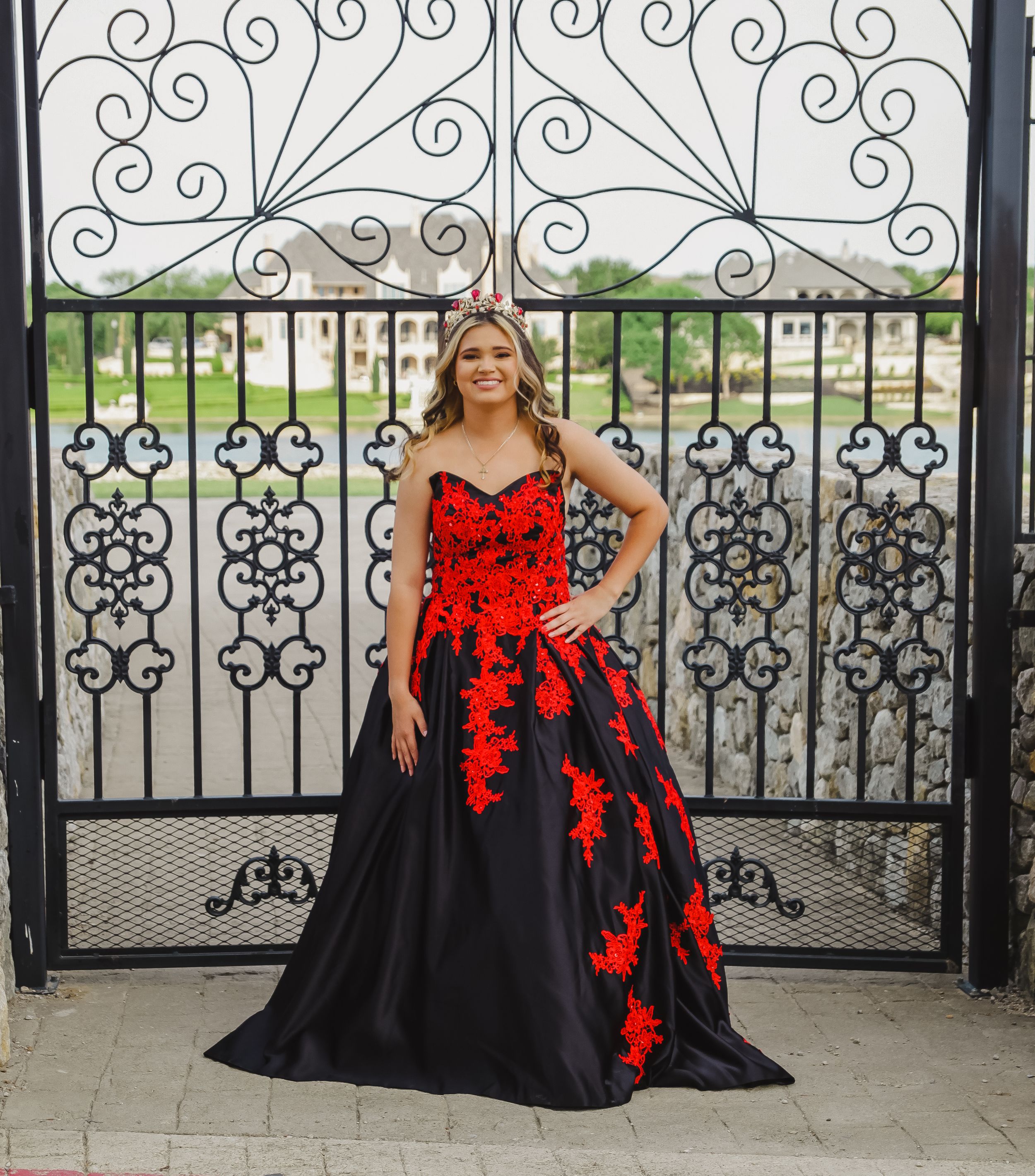 An ornate black iron gate with scrollwork designs frames a dramatic black and red gown.
