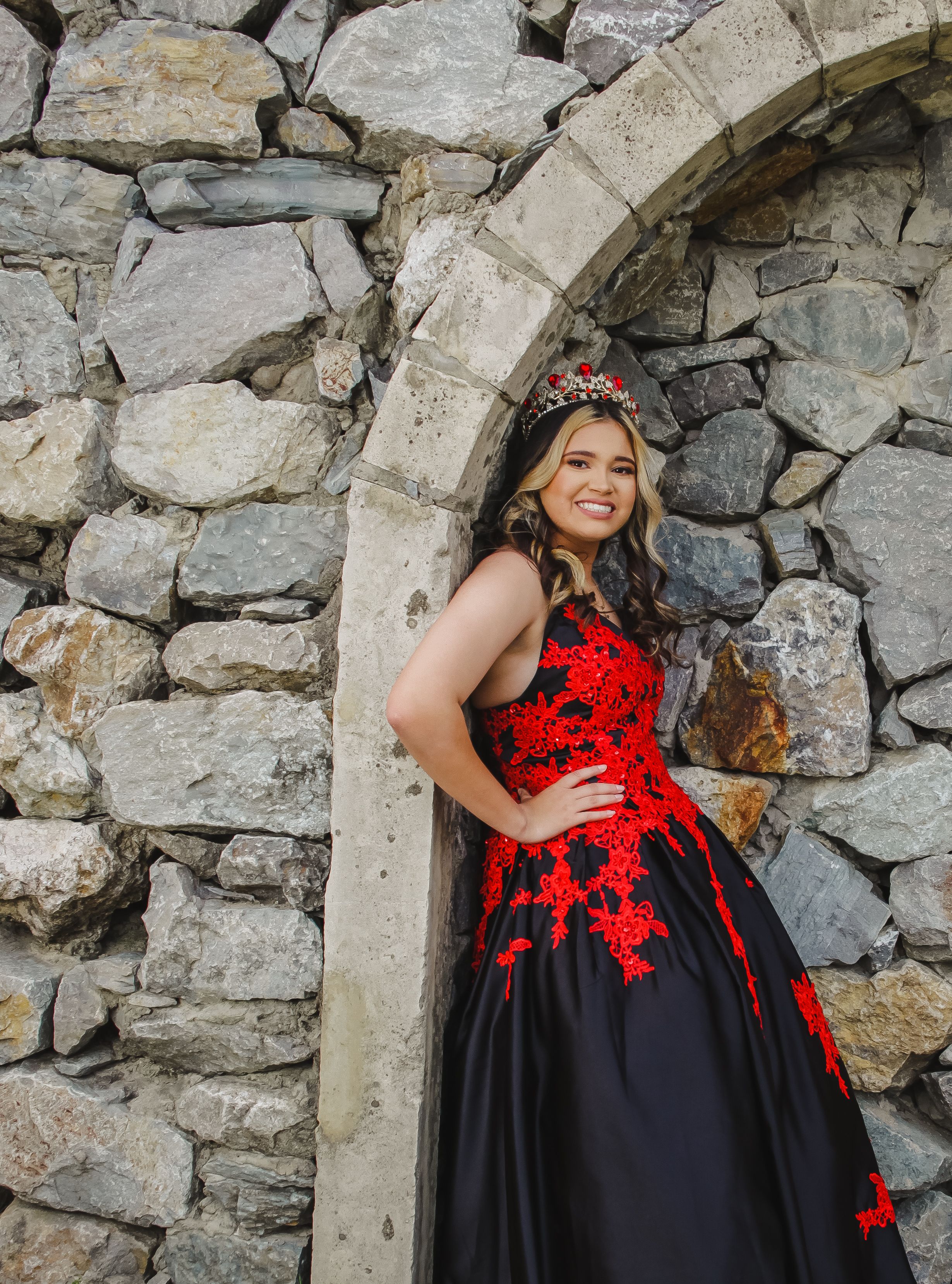 Black and red lace ball gown photographed against rustic stone wall.