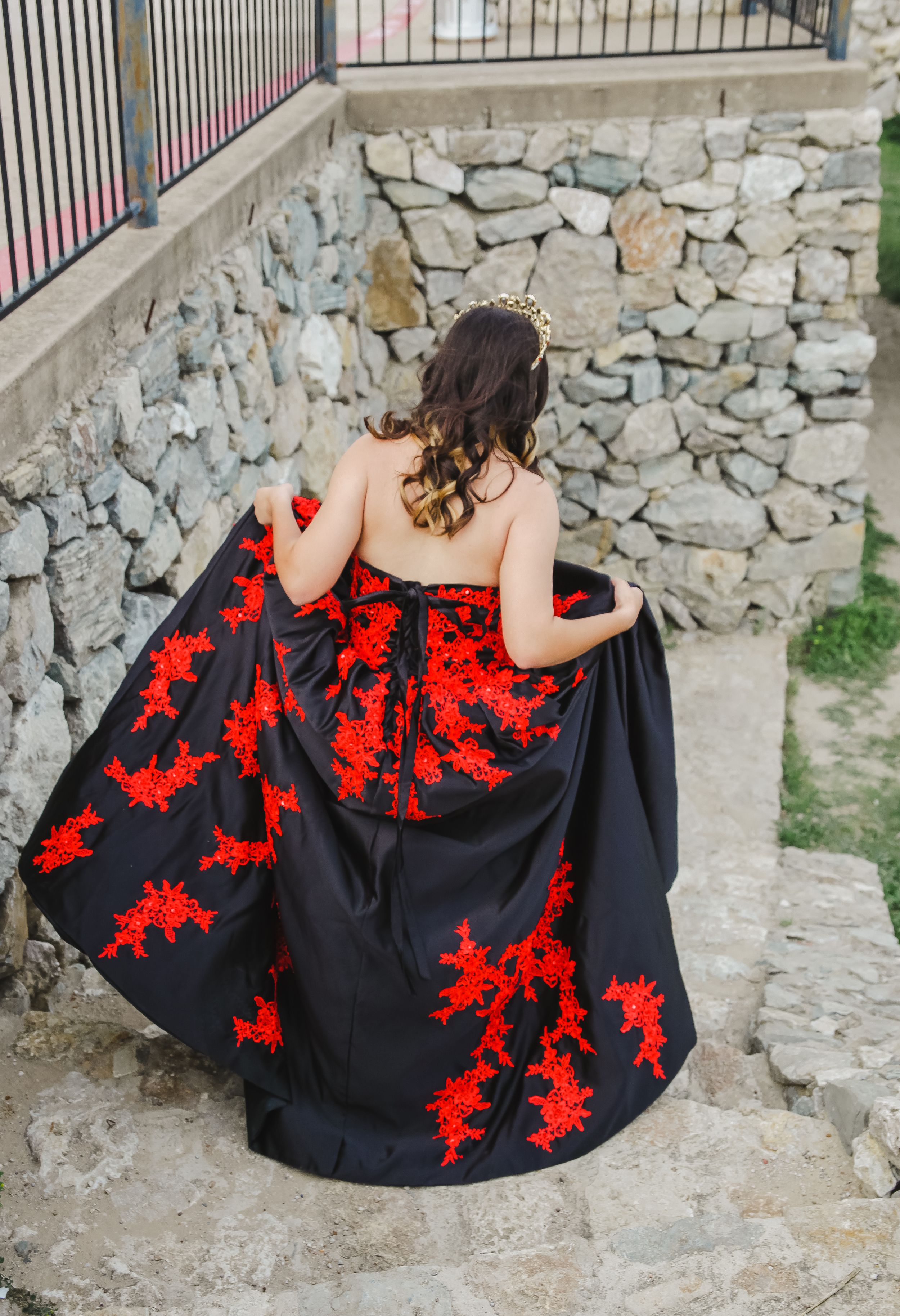 A black dress with vibrant red floral embroidery details displayed against a stone wall background.
