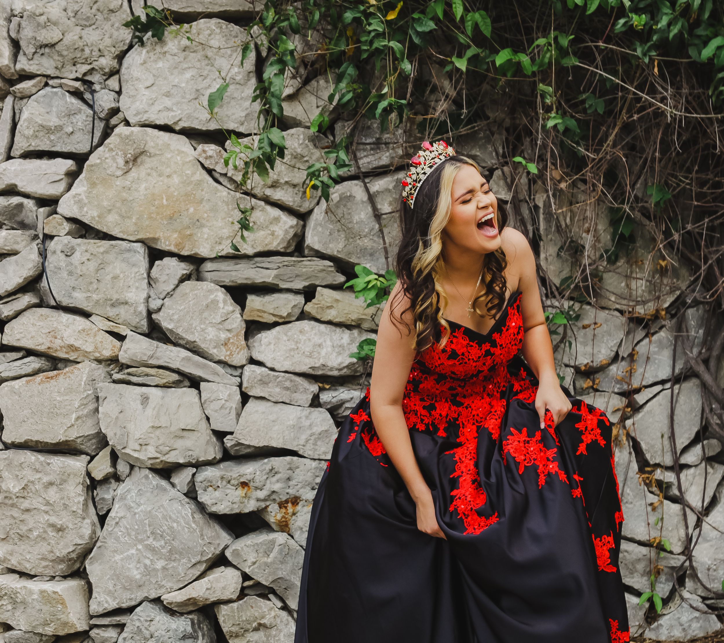 An elegant black and red dress photographed against a rustic stone wall with climbing vines.