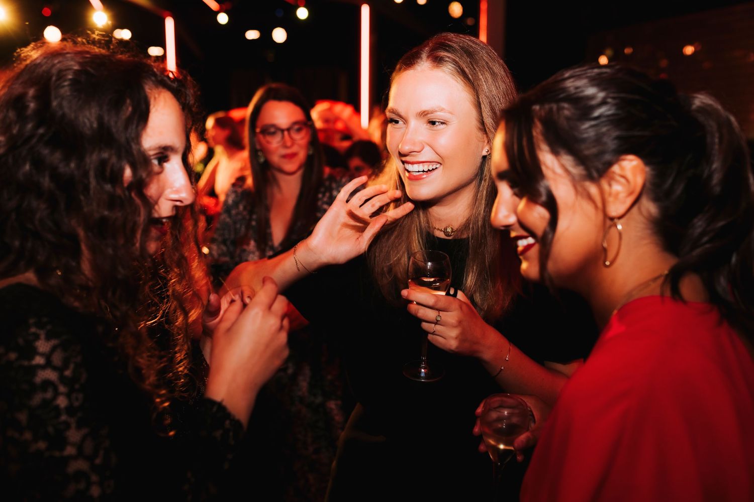 Friends sharing laughs and drinks at a festive nighttime party with string lights.