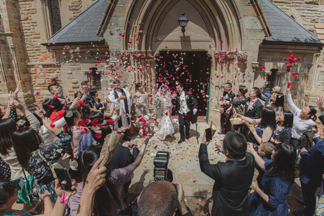 Wedding celebration with confetti shower outside historic church entrance.