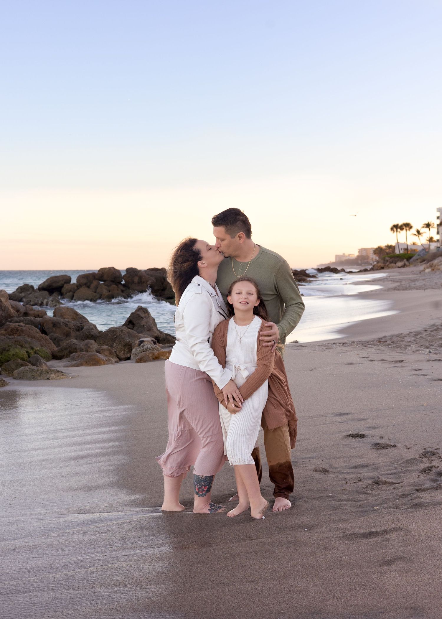 Family embracing on rocky beach at sunset during casual outdoor photo session.