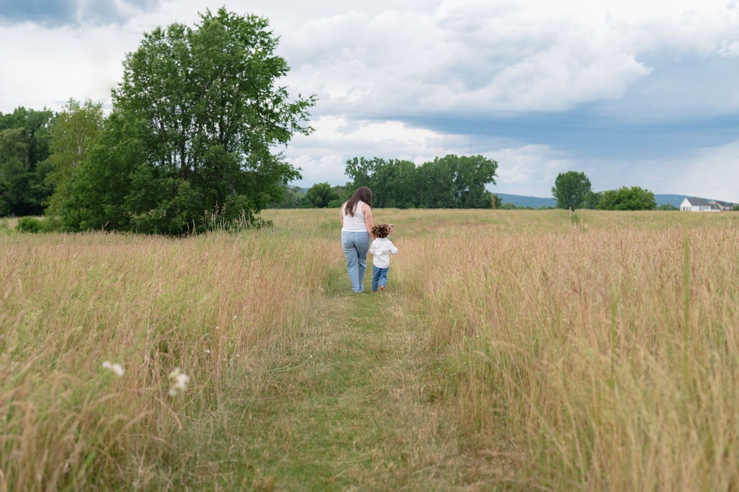 Two people walking through a tall grass meadow on a cloudy summer day.