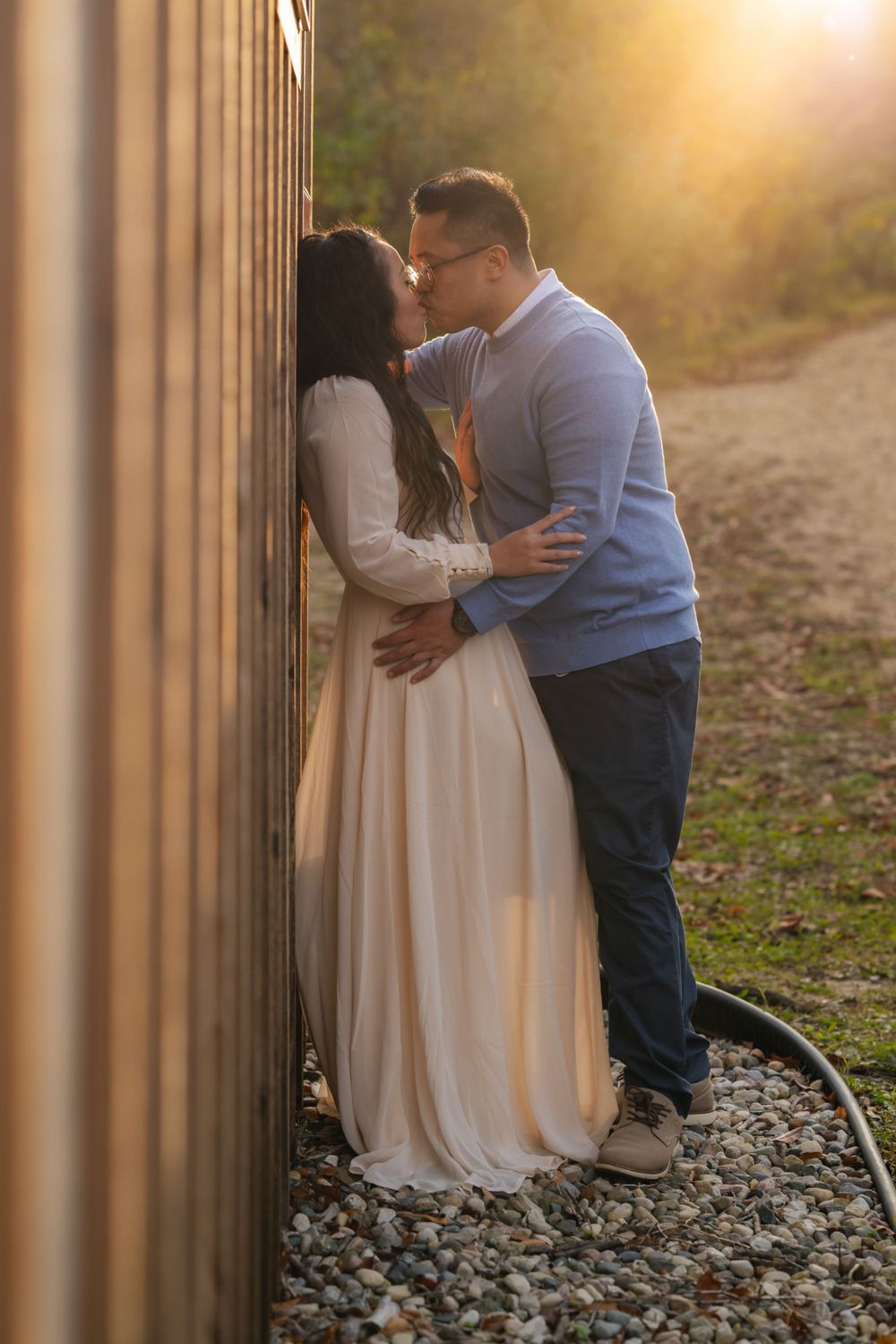 Romantic sunset engagement photo of couple embracing against rustic fence.