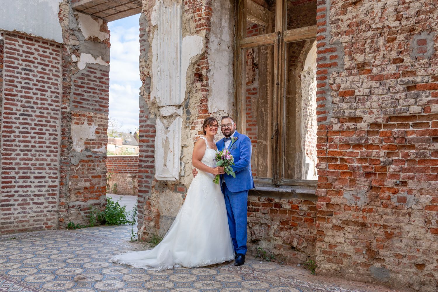 Newlyweds posing against weathered brick walls and ornate tiled floor.