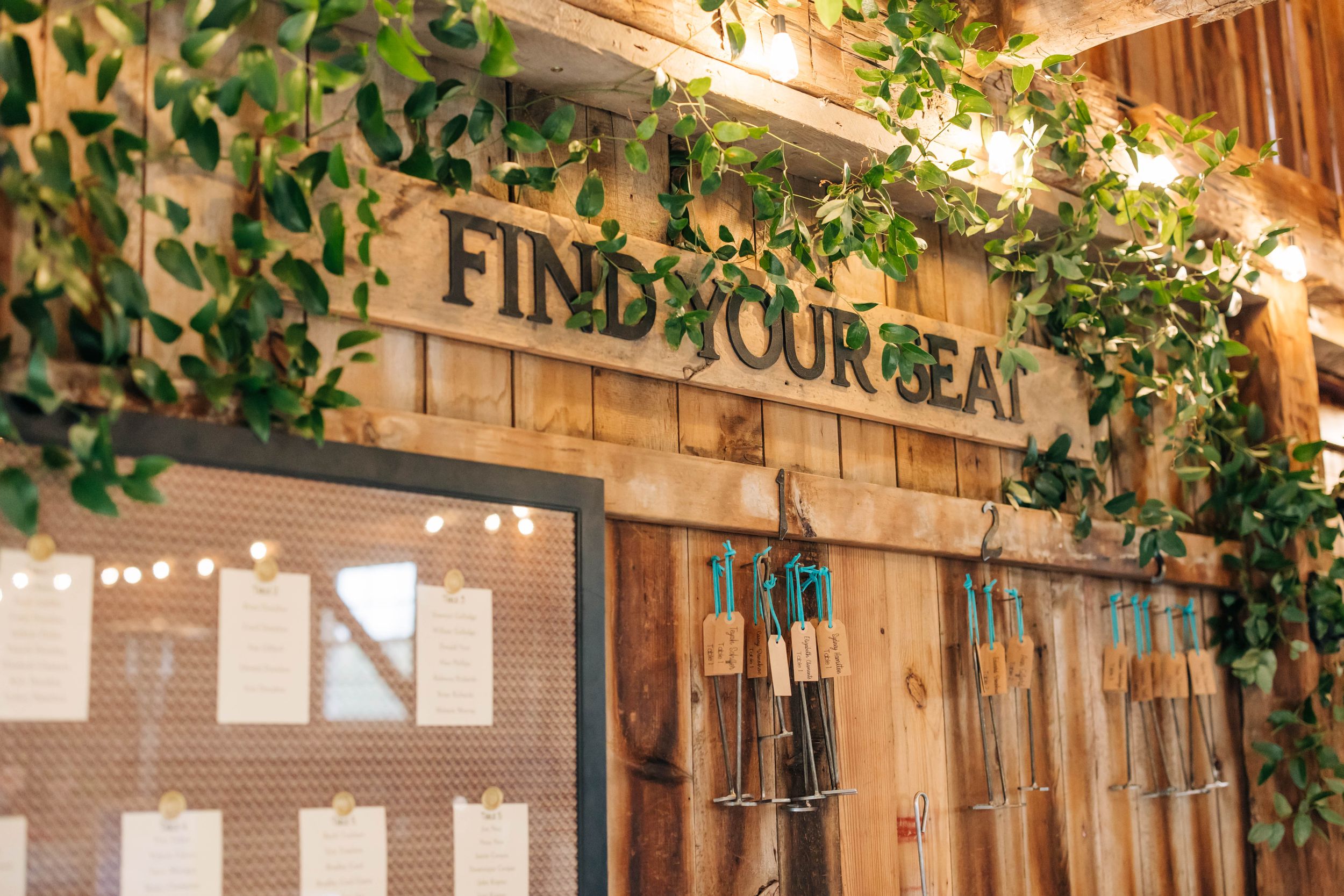 Rustic wooden barn wall with 'Find Your Seat' sign and hanging greenery decorations.