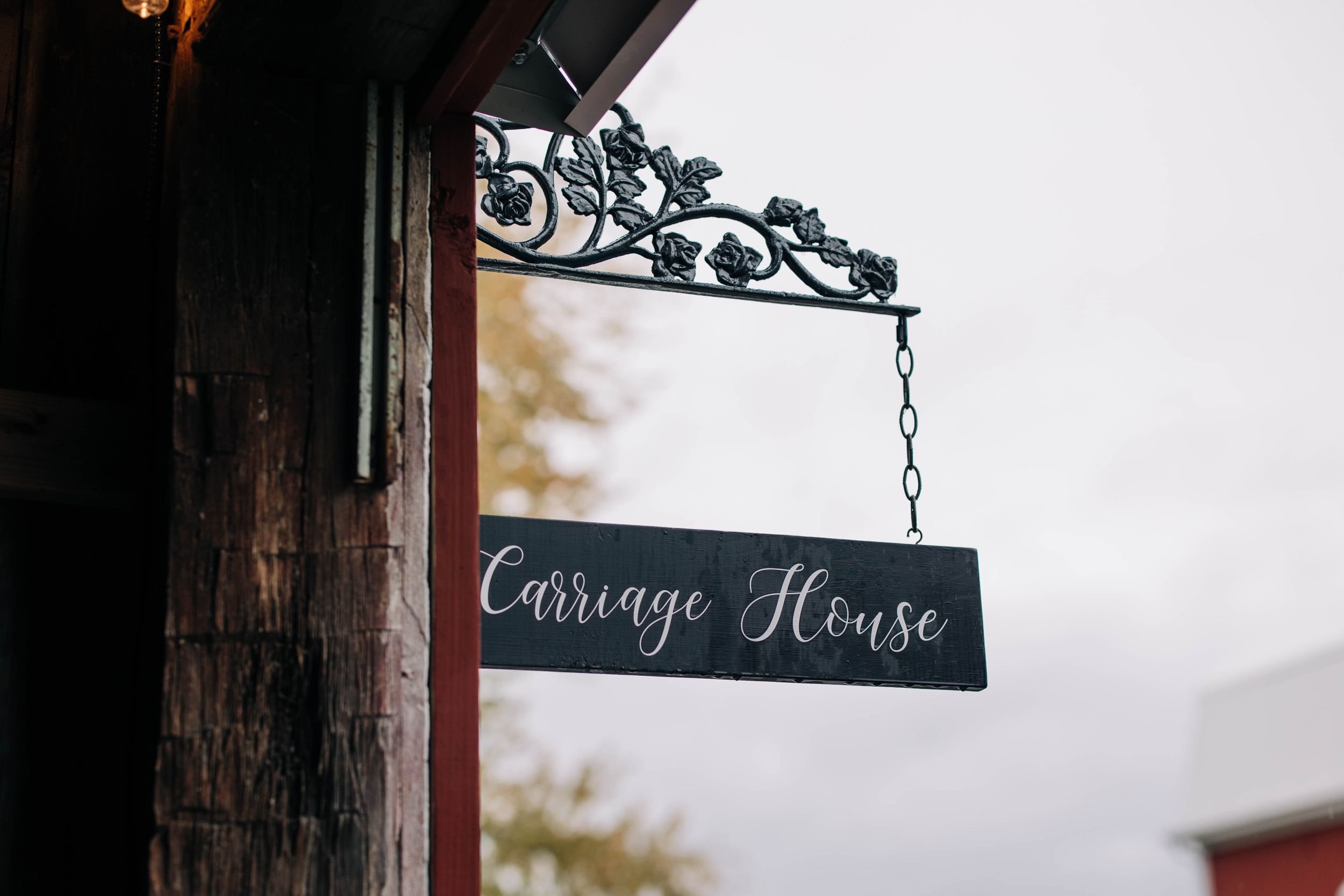 Black hanging carriage house sign with decorative metal bracket mounted on wooden wall.