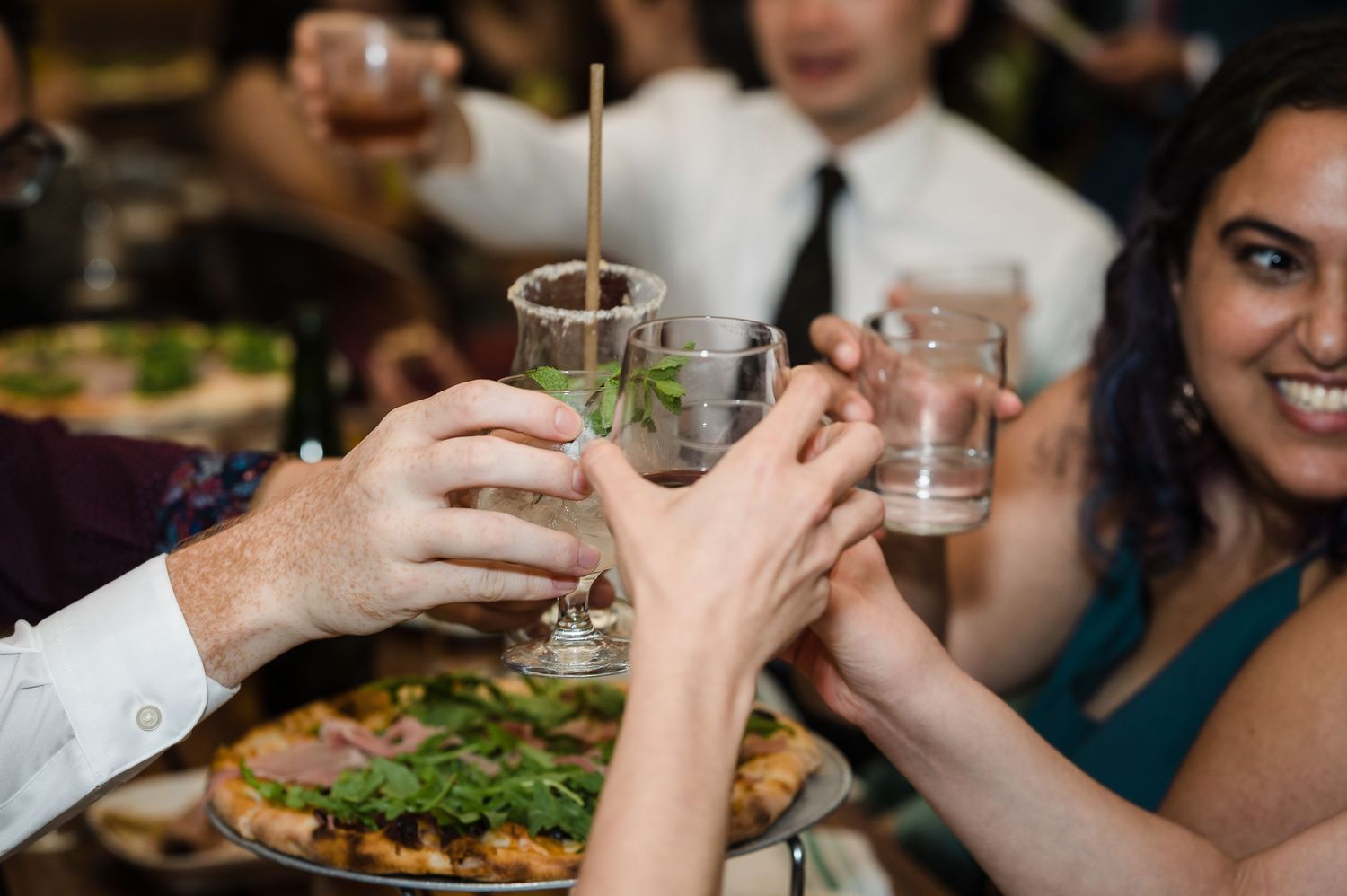 Hands raise cocktail glasses in a celebratory toast during a festive dinner party.