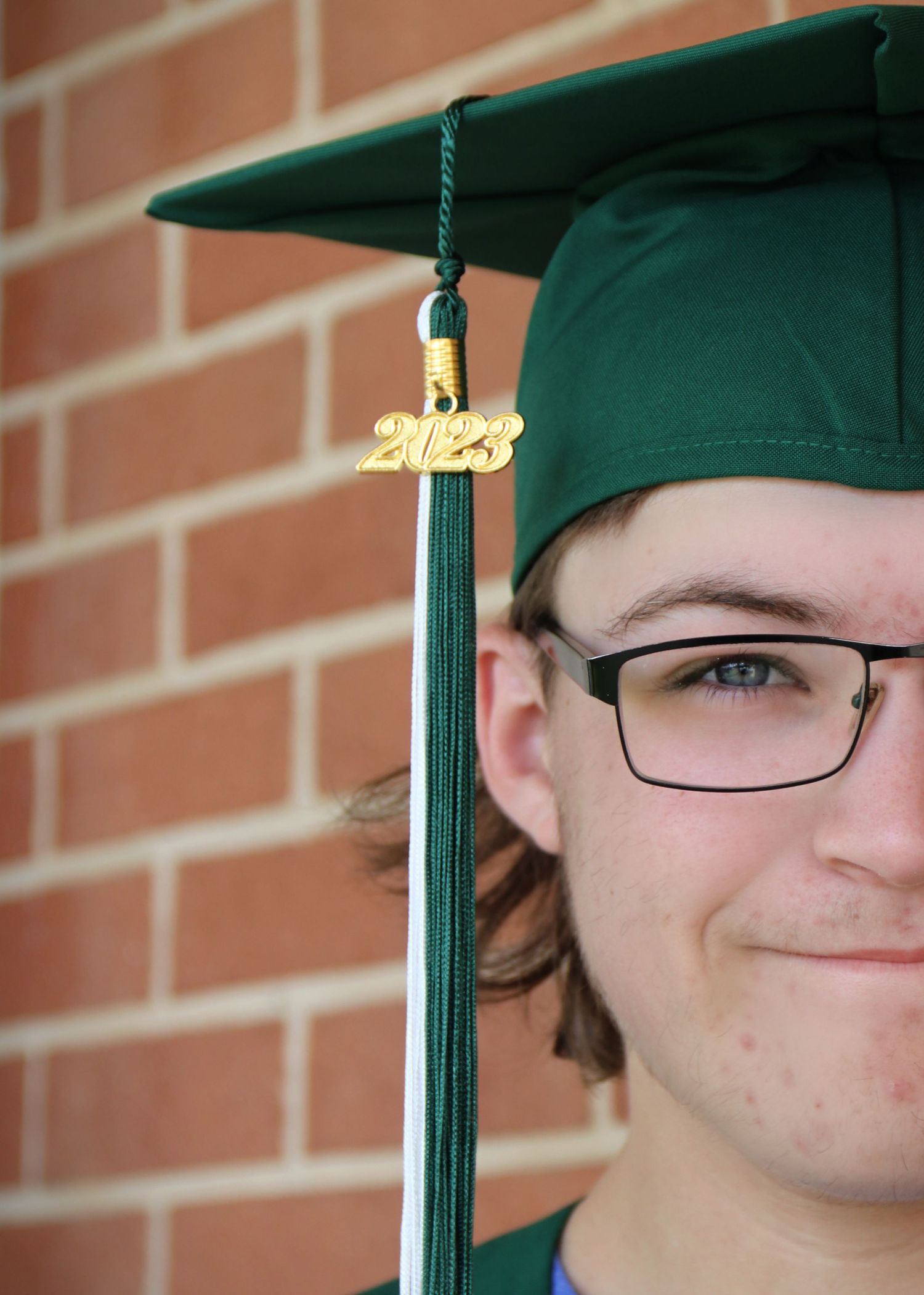 Close-up of graduation cap with 2023 tassel against brick wall background.