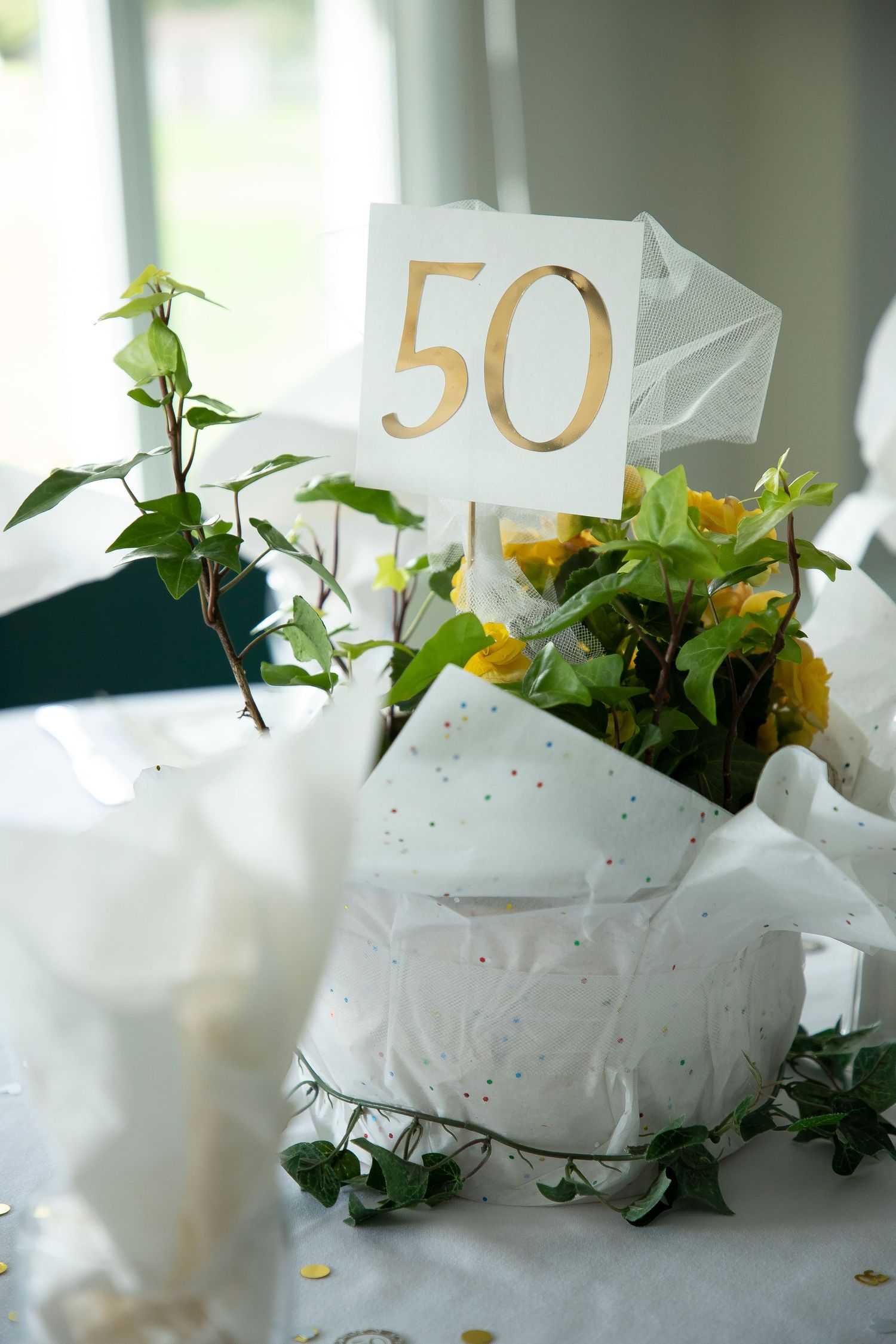 An event photograph of a table centrepiece; potted flower with a sign that says 50