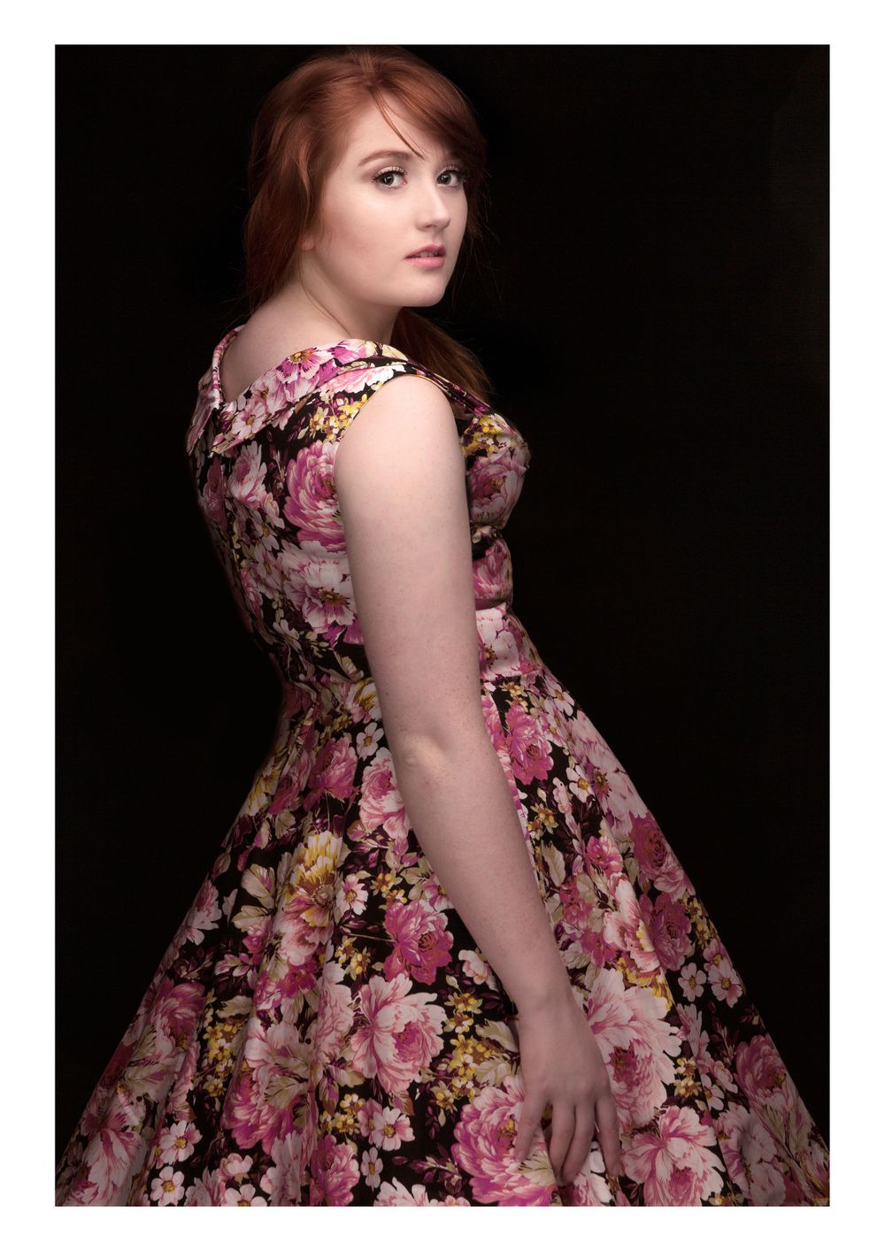 Studio portrait of someone wearing a vintage-style floral dress against a dark background.