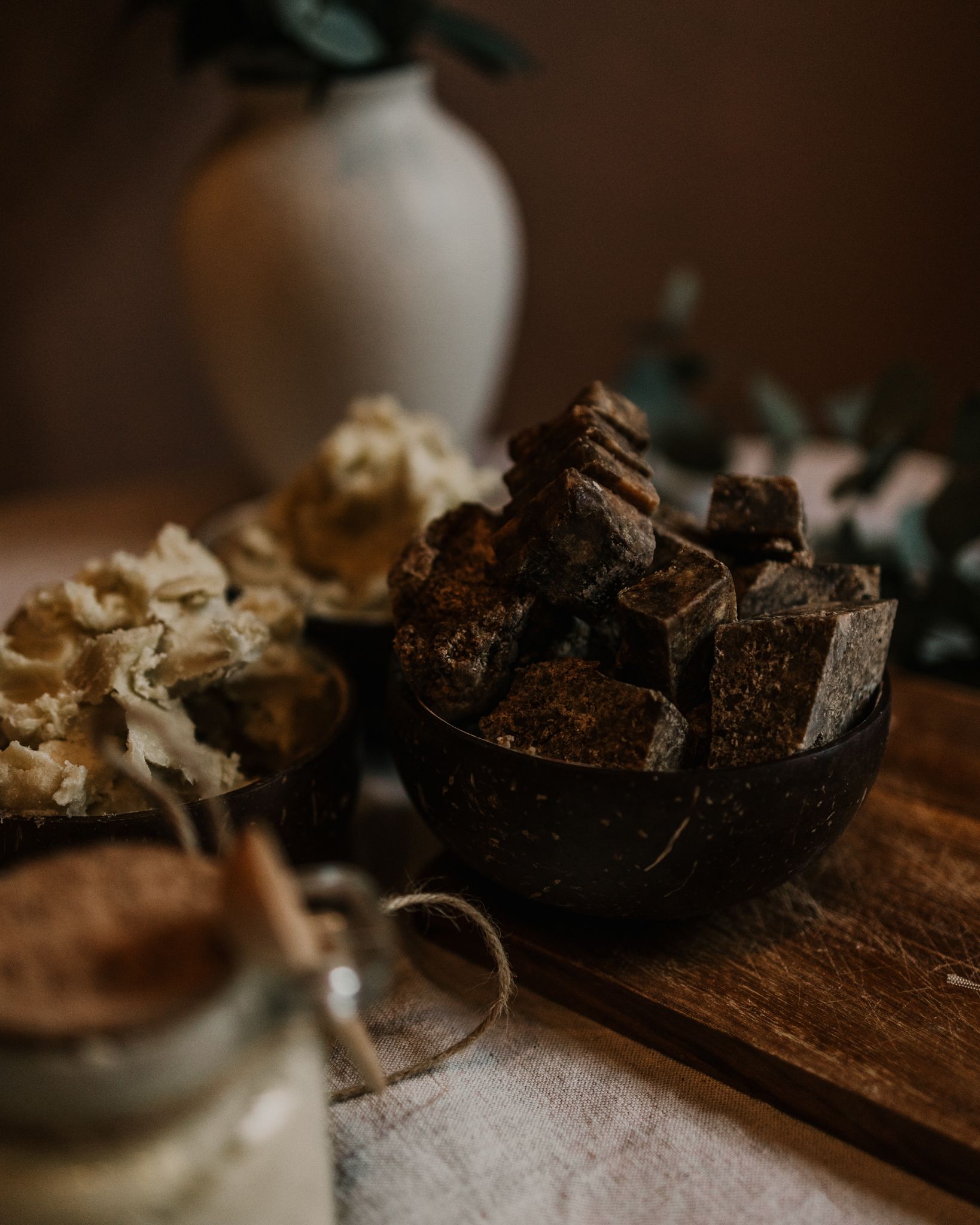 Dark stones and minerals displayed with eucalyptus in ceramic vessels on wooden surface.