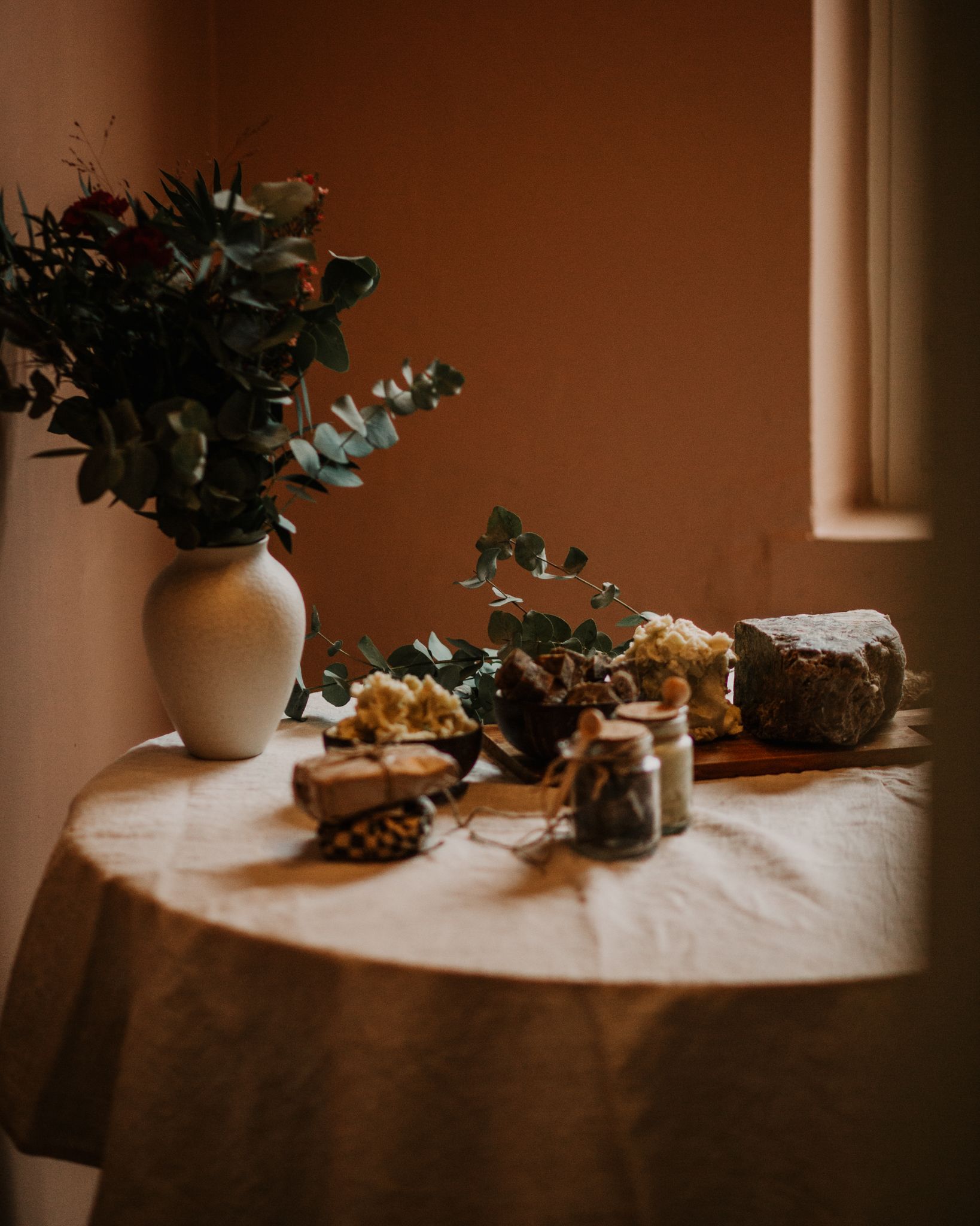 Rustic still life with vase, eucalyptus branches and objects on cloth-covered table.