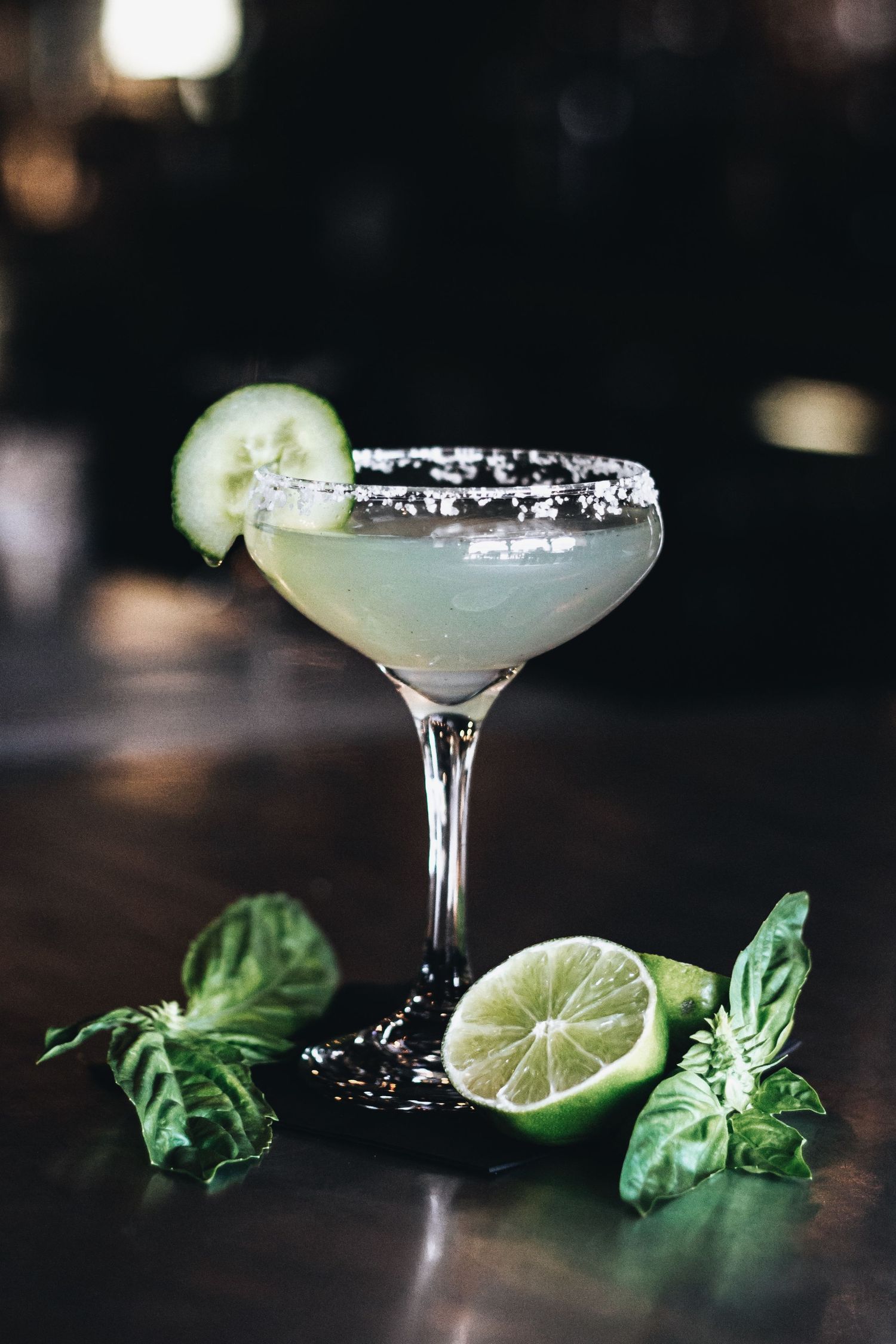 Cucumber margarita cocktail with salt rim garnished with fresh basil and lime.