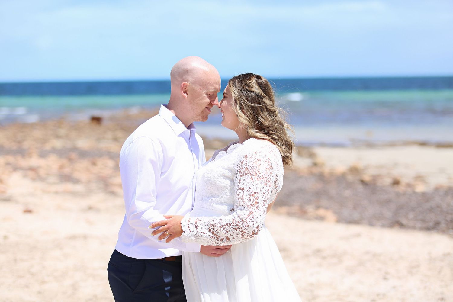 bride and groom holding each other on the beach overlooking the water
