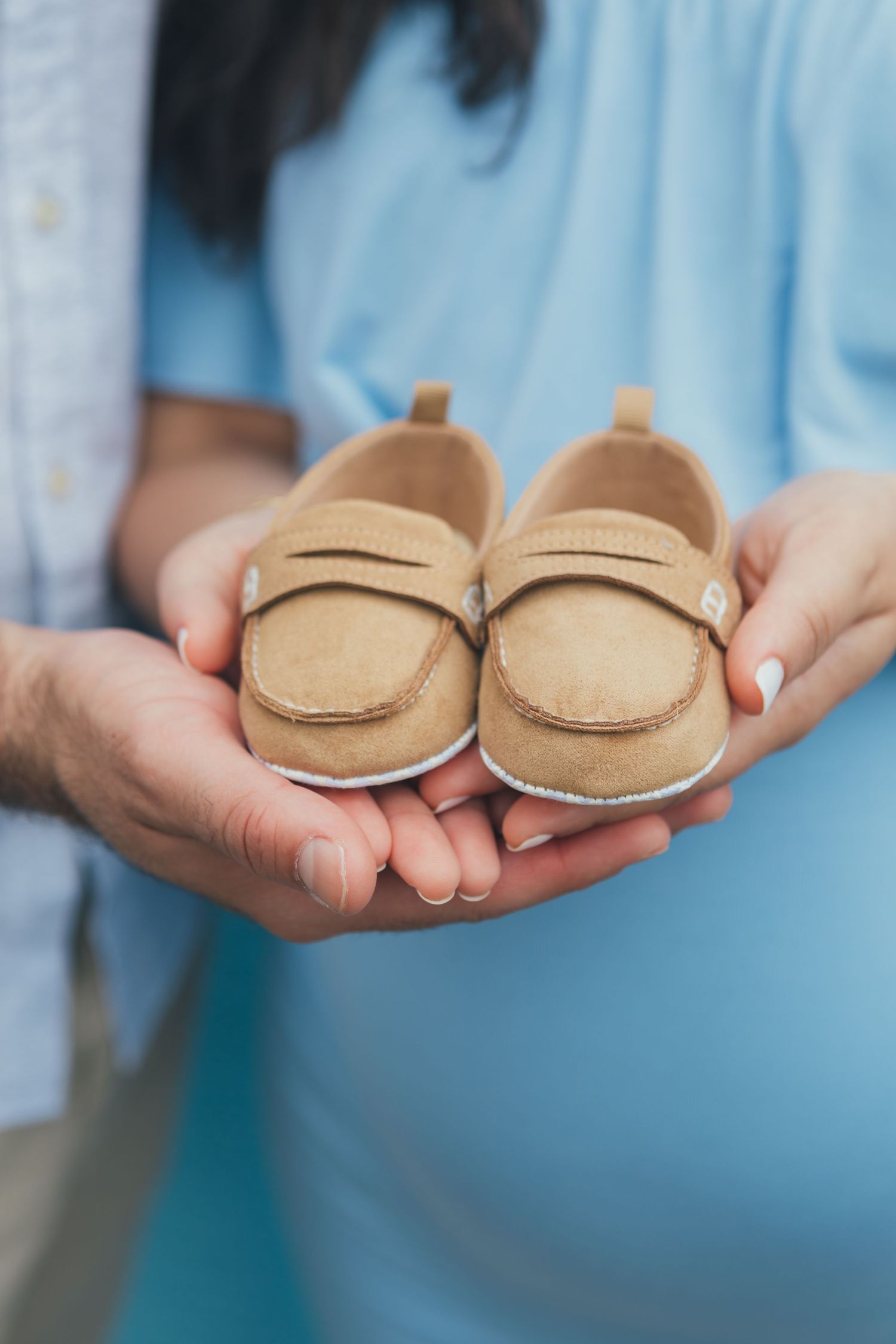 Paula Ortiz captures a close-up of the couple's hands cradling baby shoes, a heartfelt symbol of the journey ahead