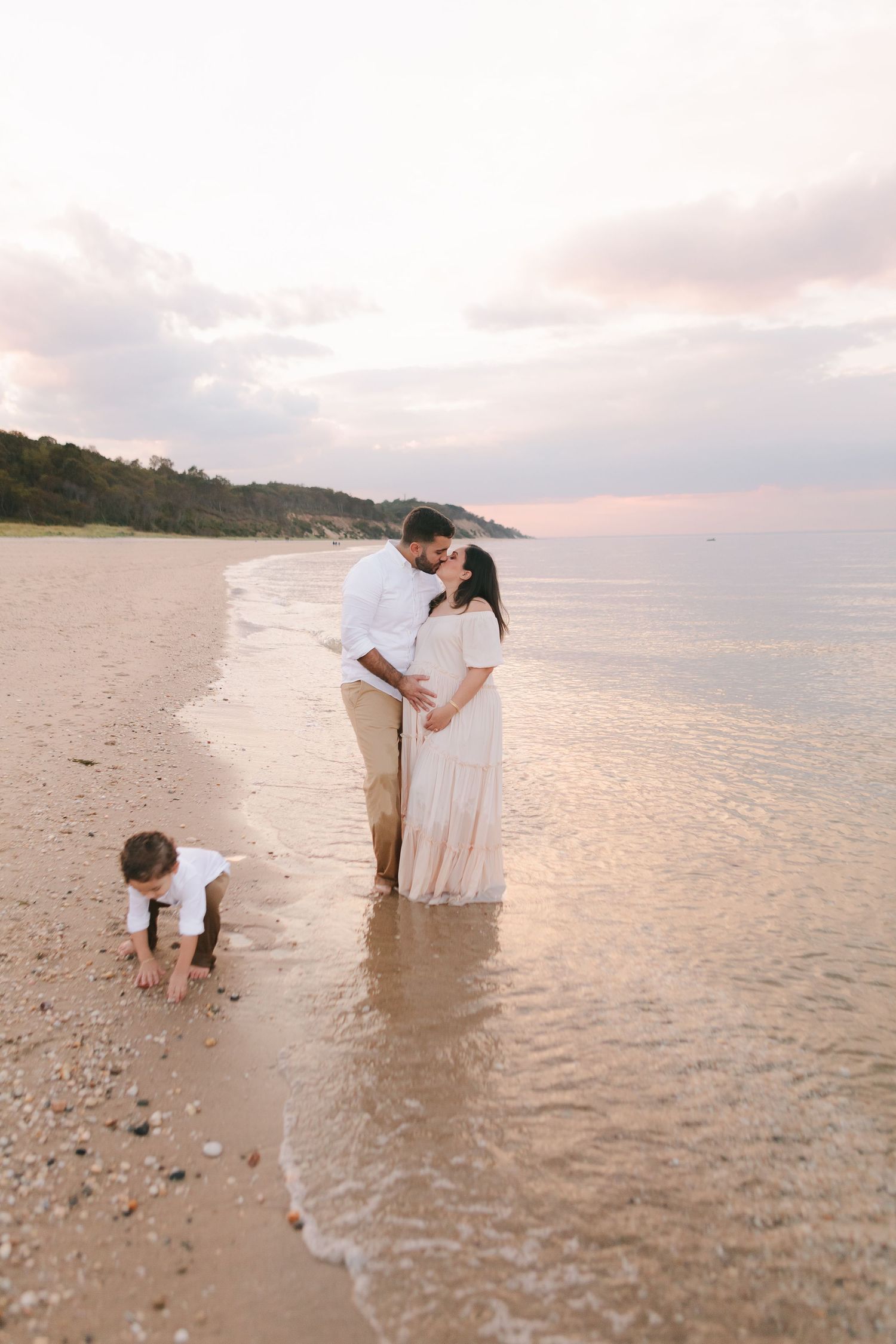 Paula Ortiz freezes a cherished moment with mom and dad kissing, their son gleefully playing in the sea behind them